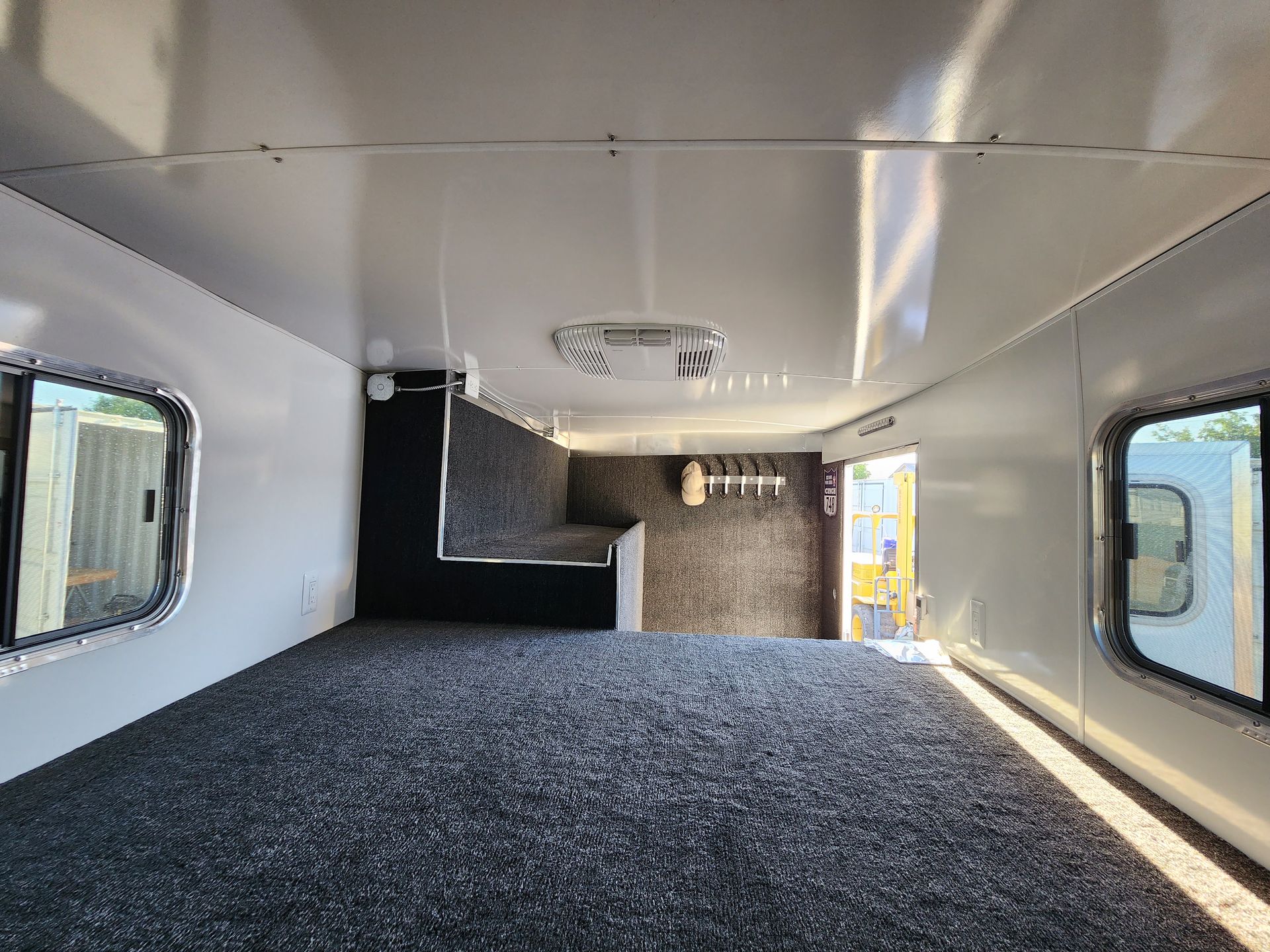Interior of a horse trailer, showing white walls and ceiling, carpeted floor, windows, and storage.