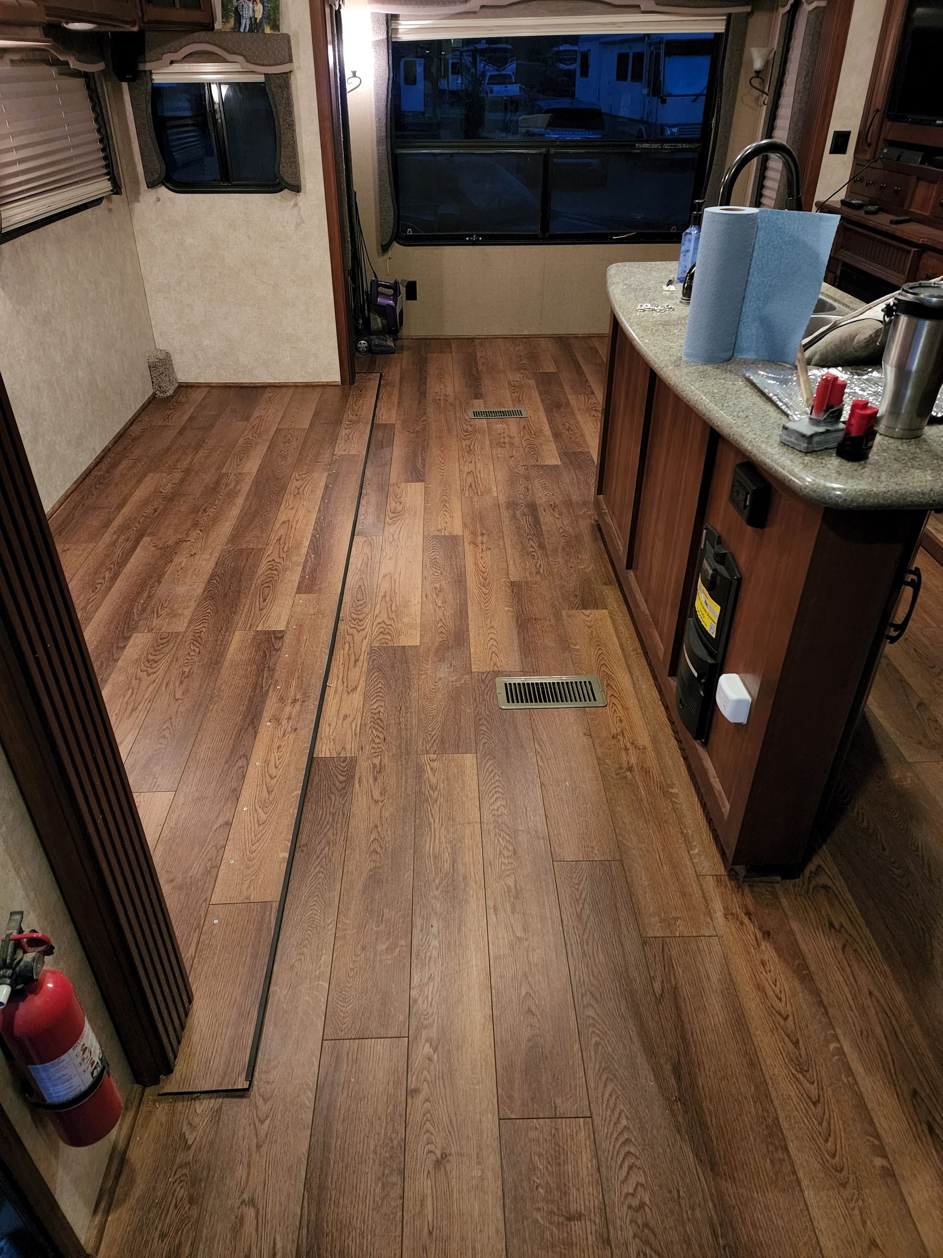 RV interior with new wood-look flooring and a kitchen island, fire extinguisher visible.