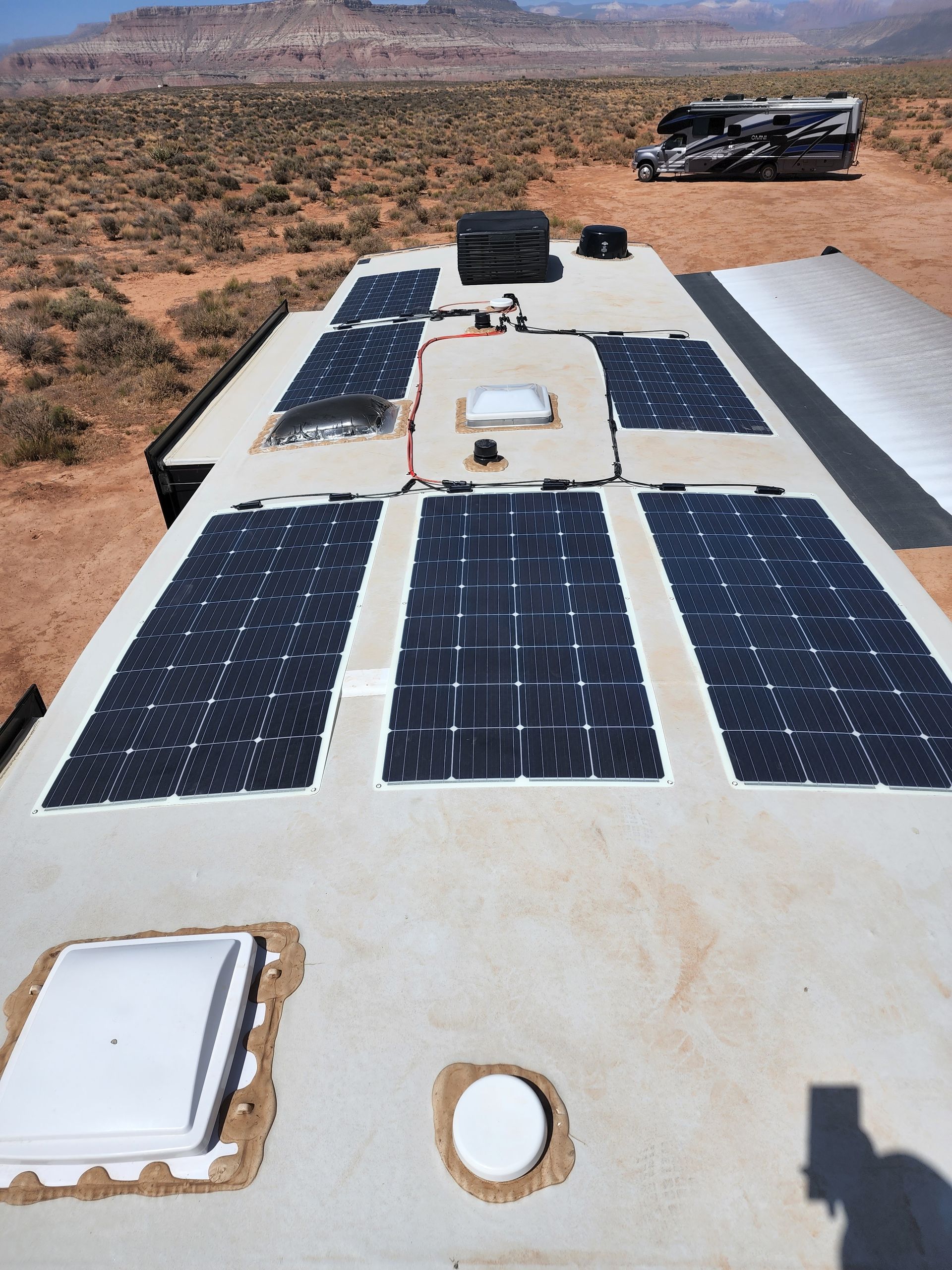 RV rooftop with solar panels in a desert setting; another RV is visible in the background.