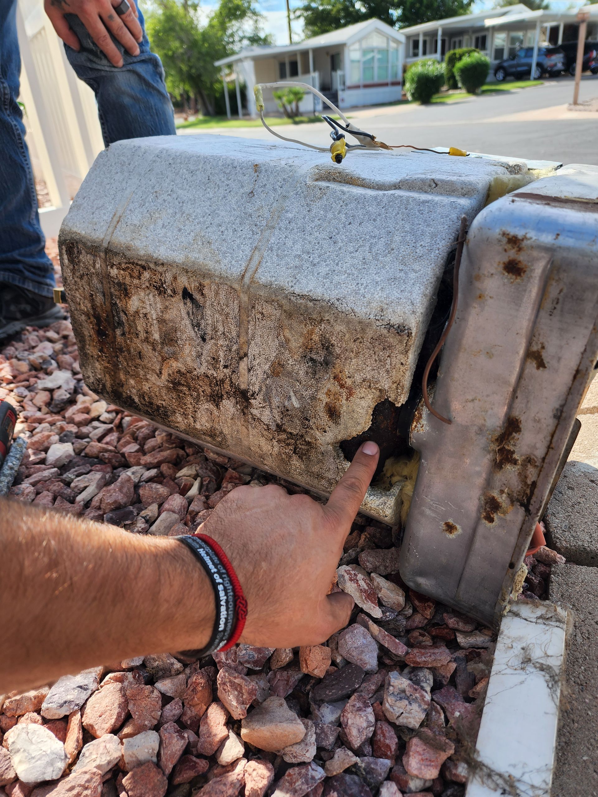 A person pointing at damaged outdoor electrical box with visible wires. Debris and discoloration on the box.