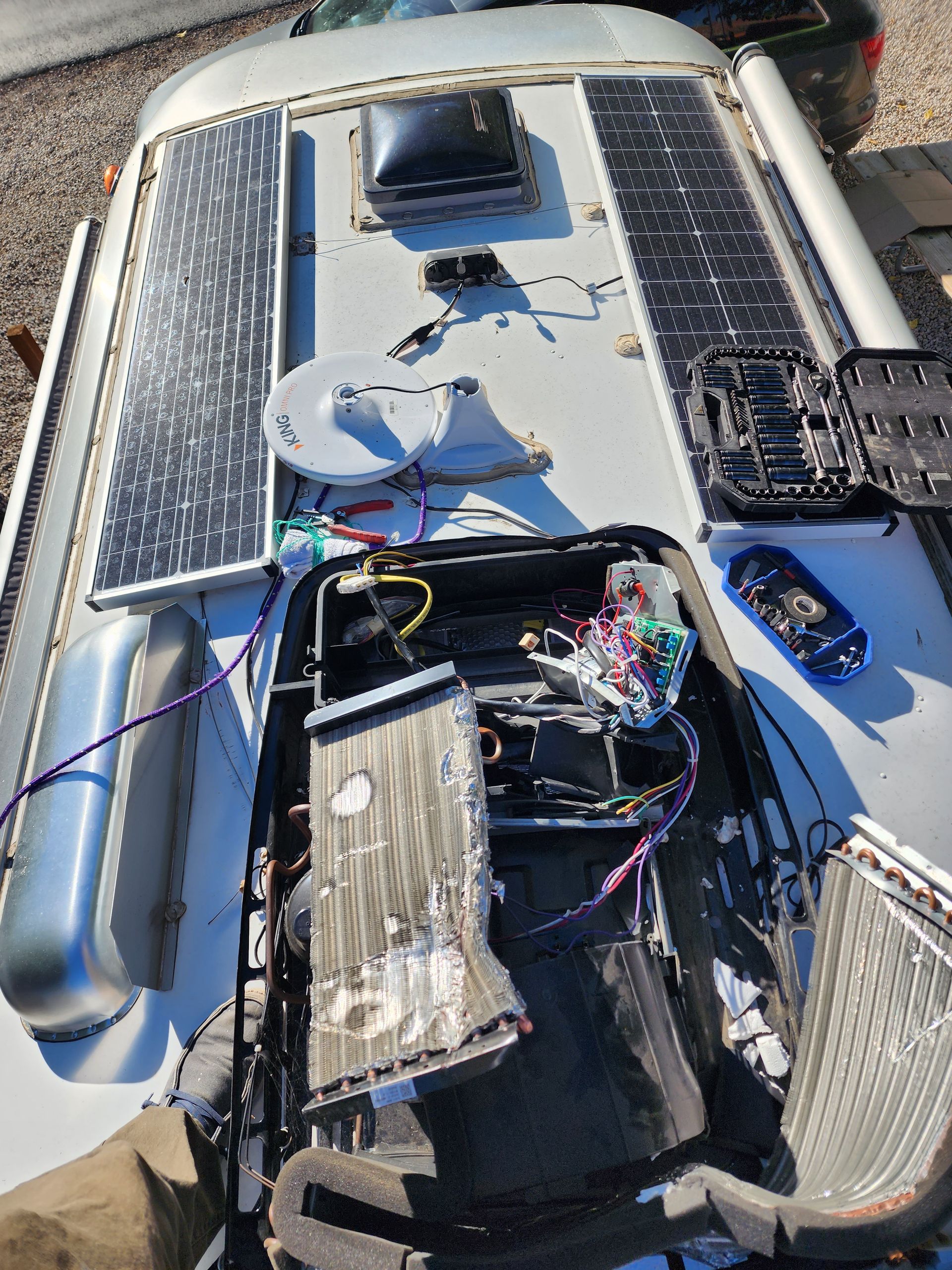 RV roof with solar panels, open compartment exposing wires and components, silver exterior.
