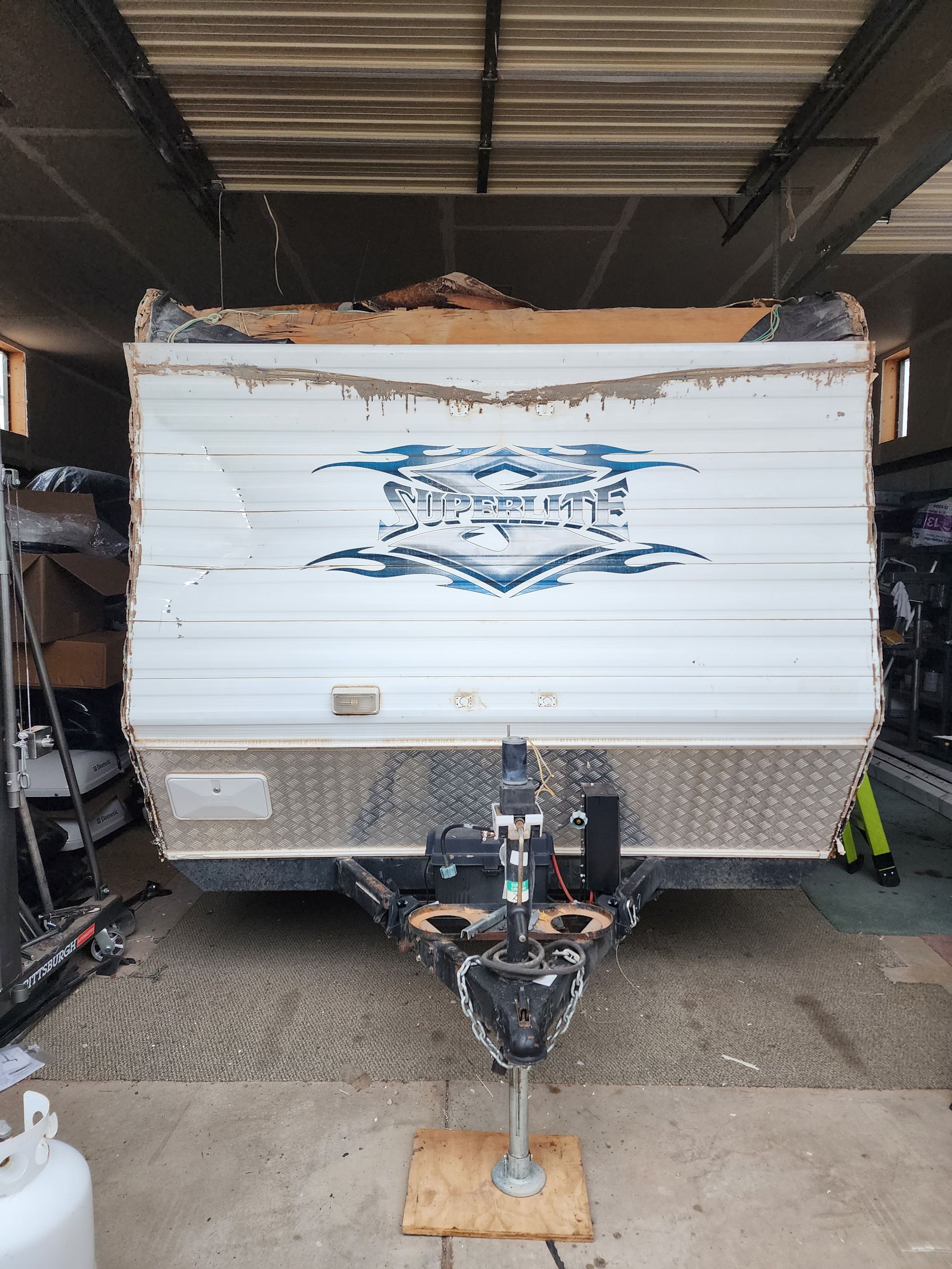 White and blue travel trailer with damage, parked inside a garage.