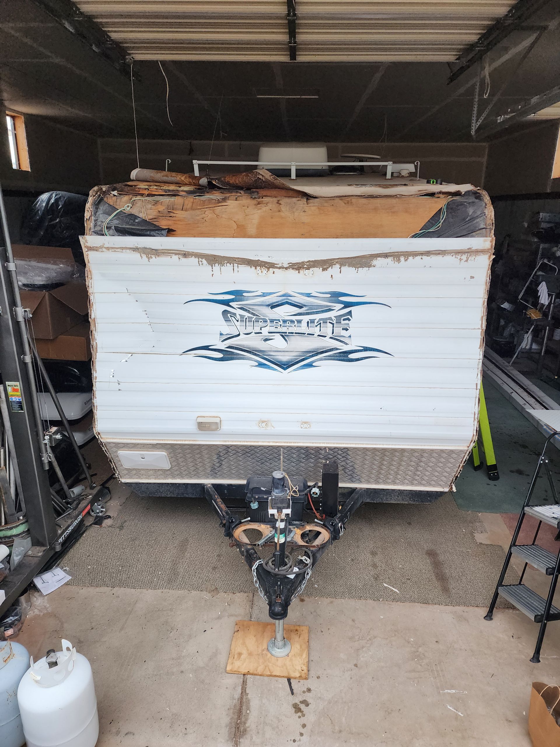 White and brown camper trailer with a damaged roof, parked in a garage.