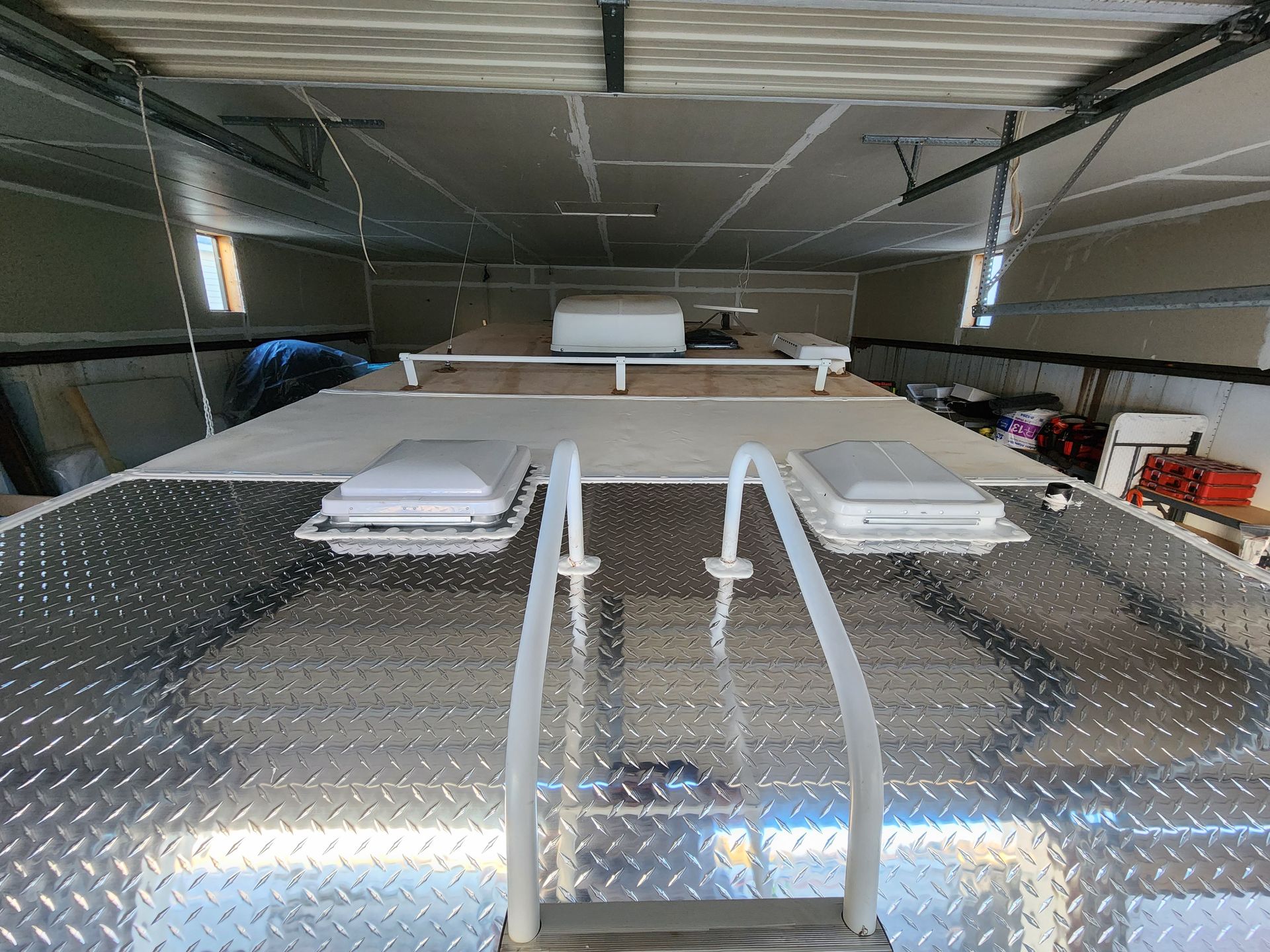 Aluminum-covered RV roof with ladder, two vents, and garage setting.