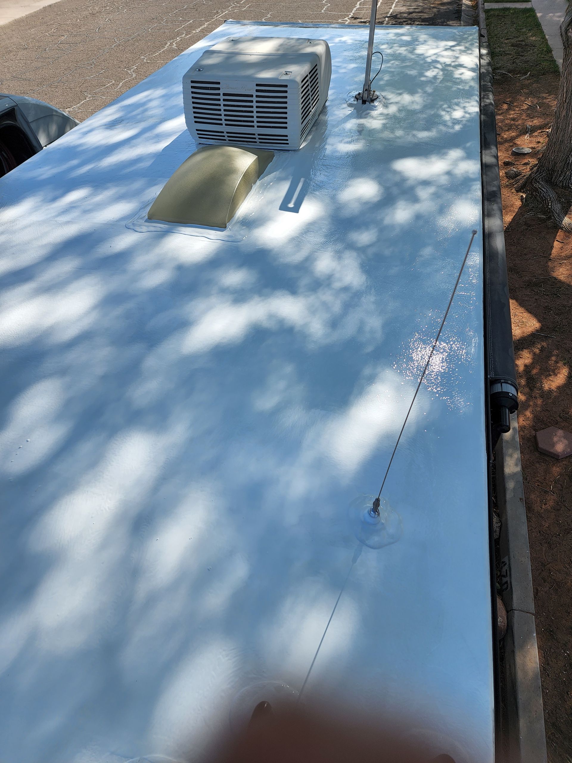 White-coated RV roof with air conditioner, vent, and antenna. Shadows cast across the surface.
