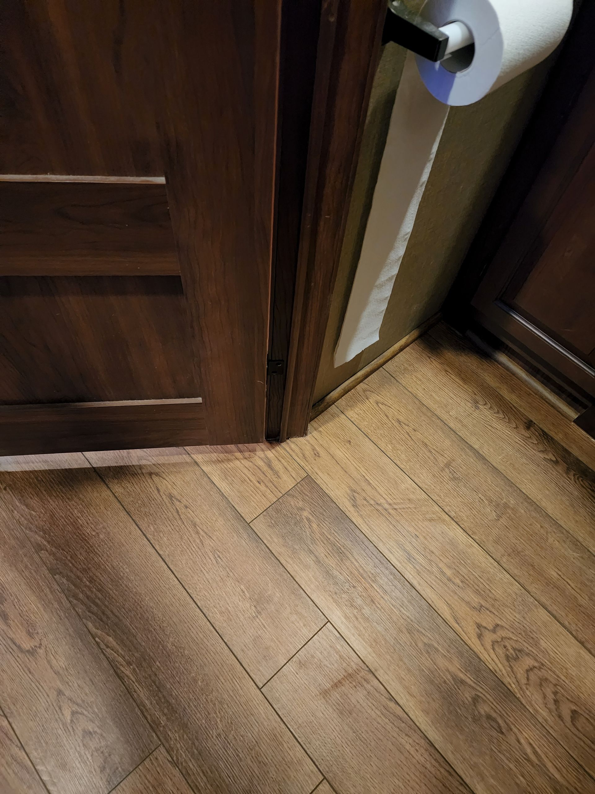 Wooden door and cabinets with wood-look flooring and a hanging roll of toilet paper in a corner.