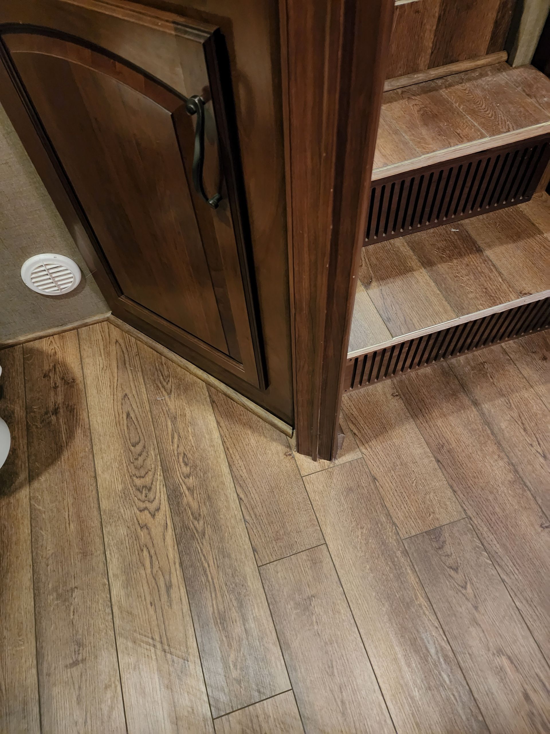 Wood-look flooring meets a cabinet and stairs in an RV. The door has a handle.