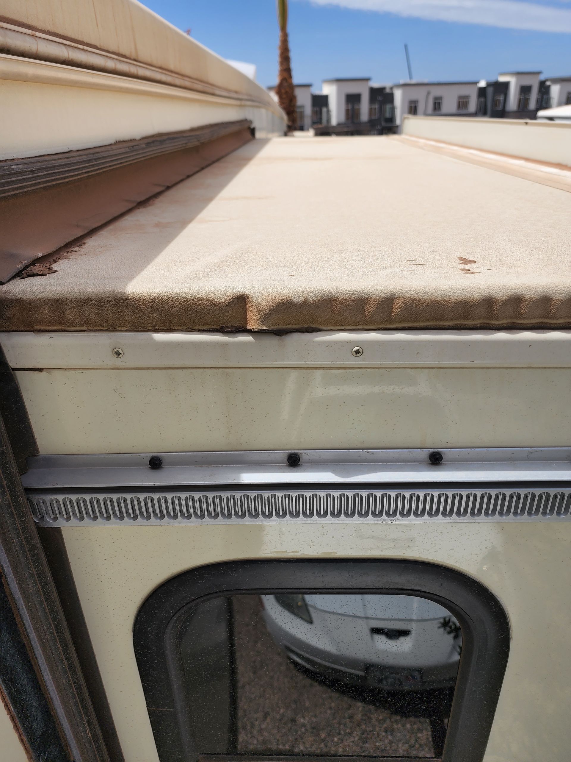 Beige vehicle roof edge with a window below, overlooking buildings on a sunny day.