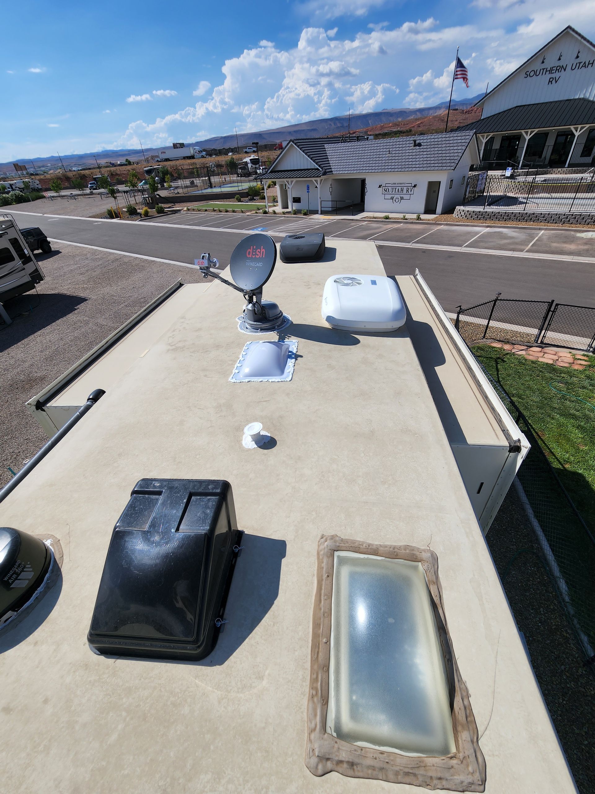 RV roof with satellite dish, vents, and skylight under a blue sky.