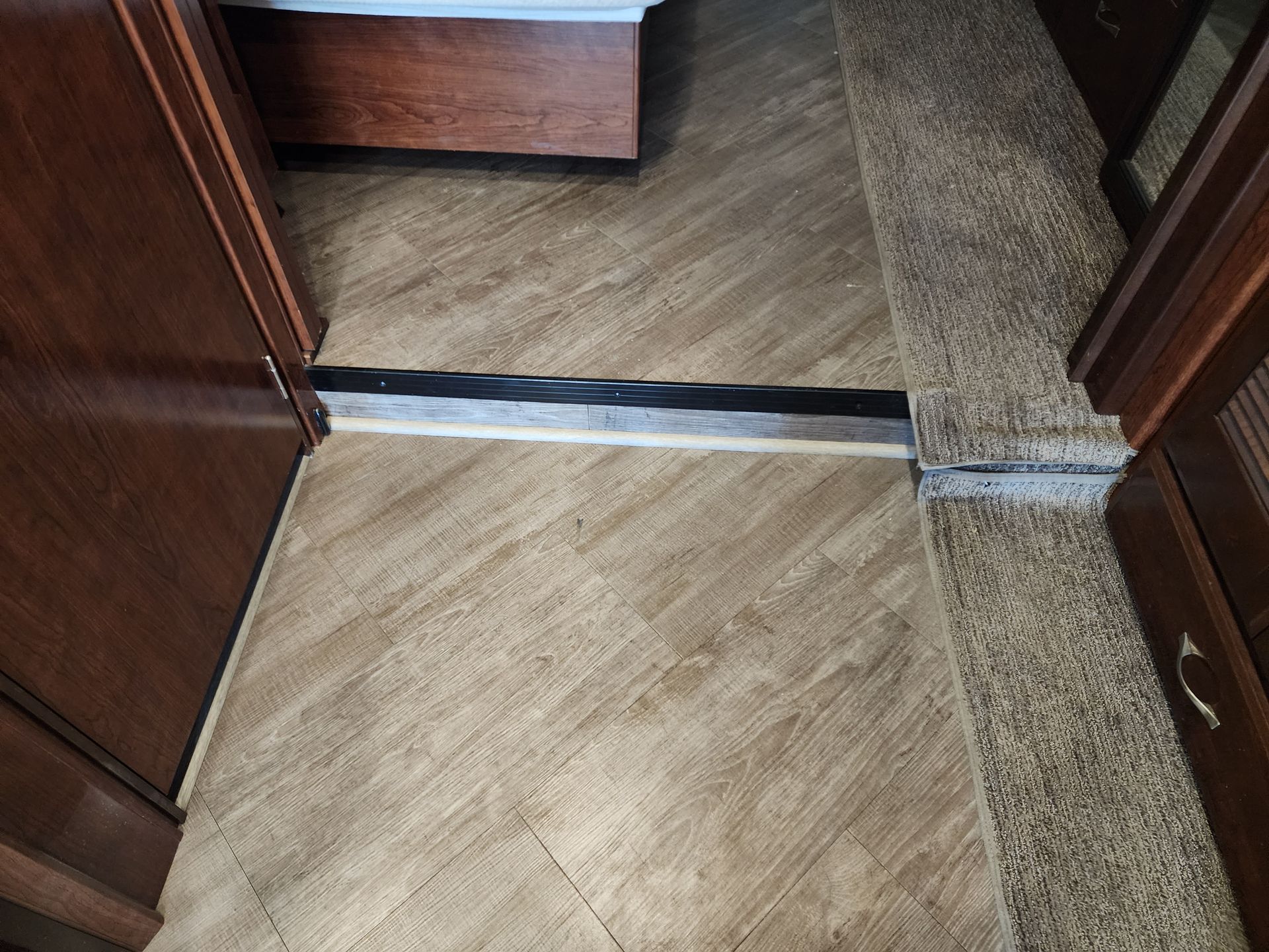 Interior RV flooring showing wood-look vinyl and carpet with a transition strip between them.