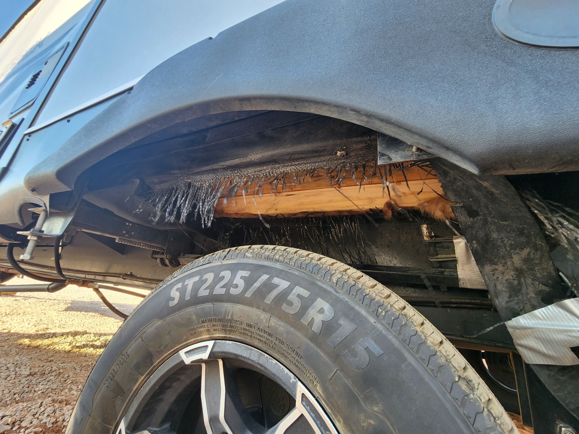 Wheel well of a recreational vehicle. Exposed wood, tire, and textured black coating are visible.