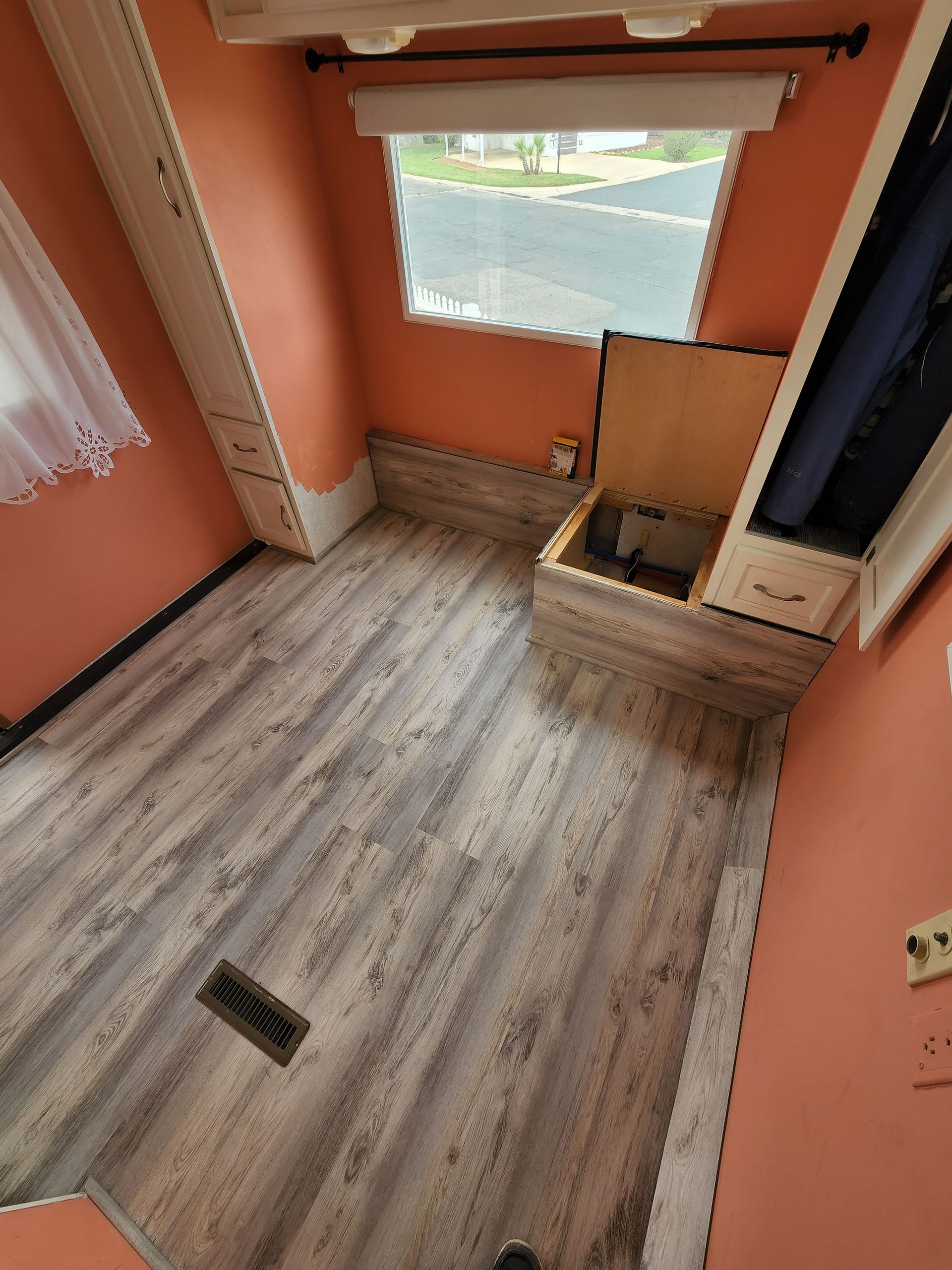 Small room with wood-look flooring, salmon-colored walls, window, built-in storage bench, and closet.