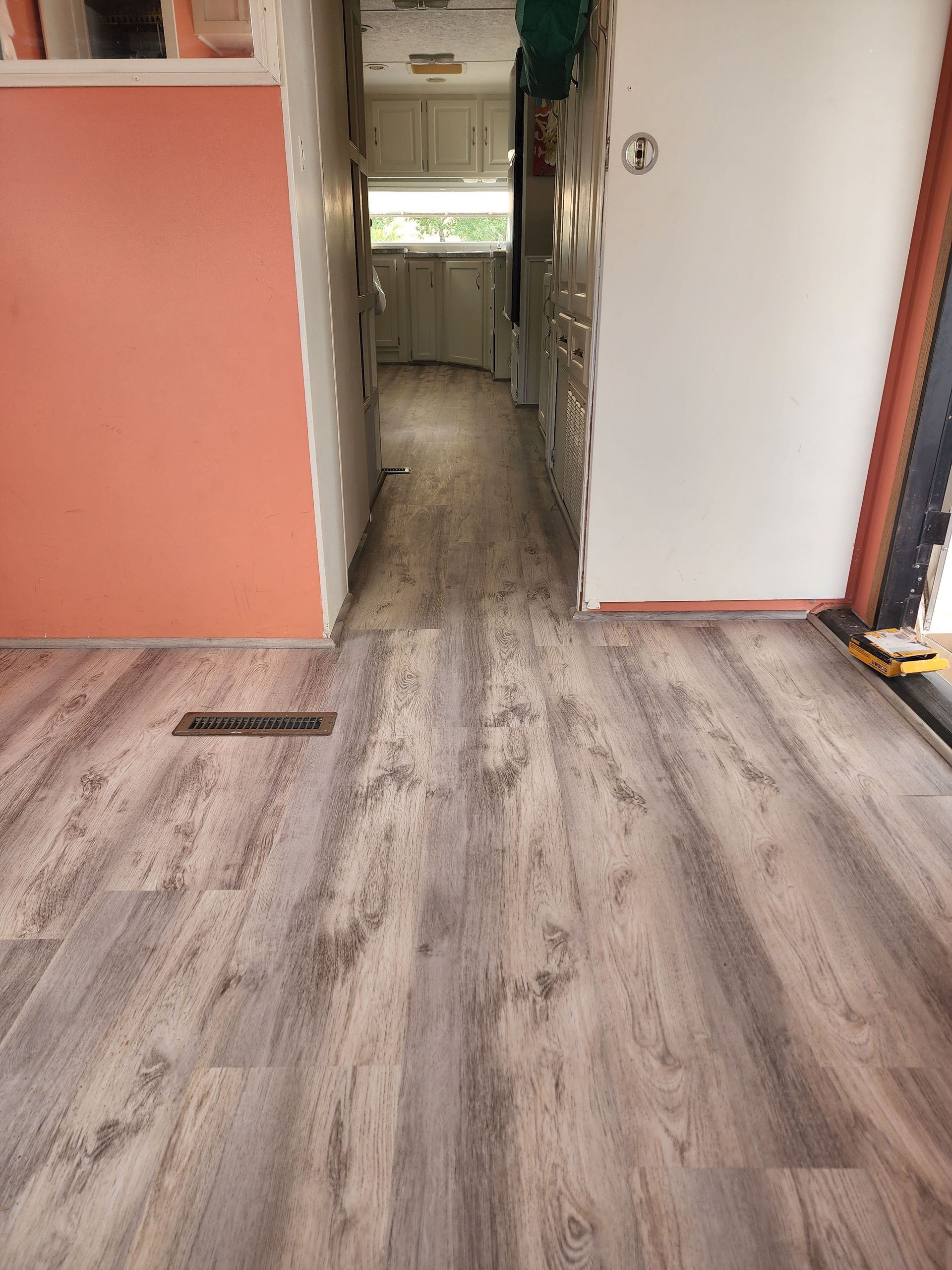 Hallway with wood-look flooring, peach and white walls, leading to a kitchen with cabinets.