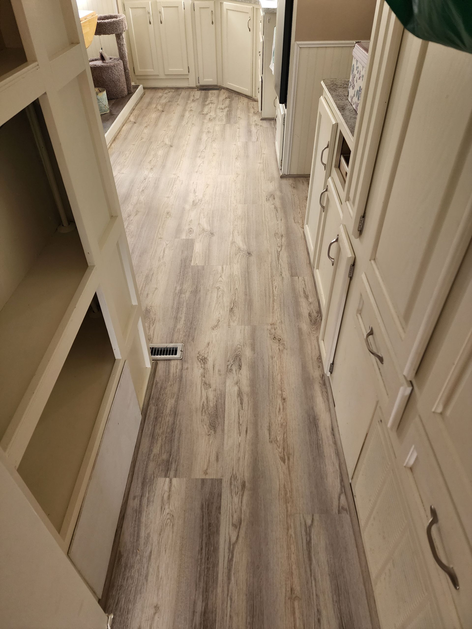 Narrow kitchen with light wood-look floor, white cabinets and open shelving on either side.
