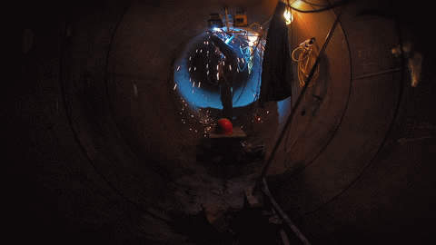 A person welding inside a large metal pipe, sparks flying.