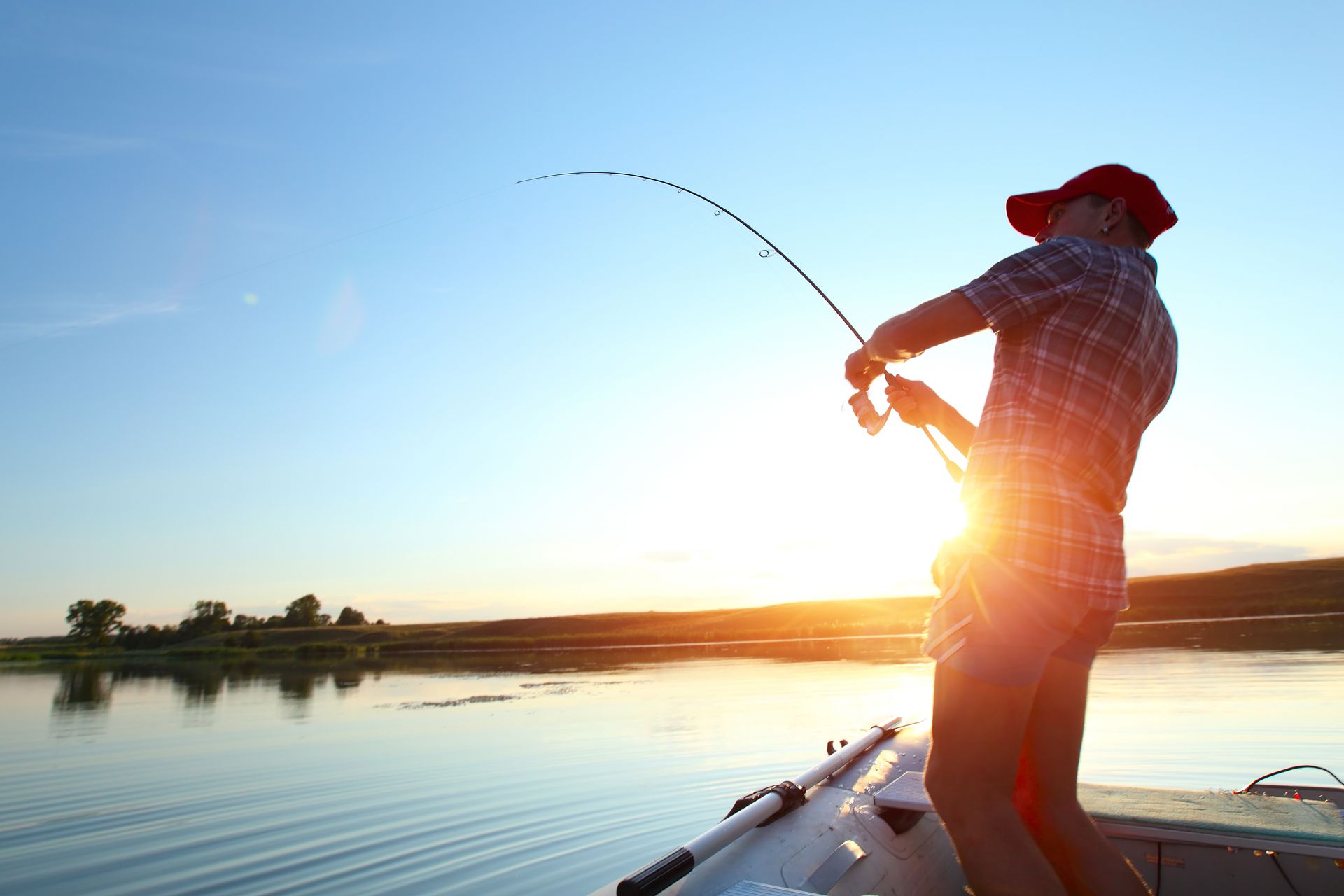A man is fishing from a boat on a lake at sunset.