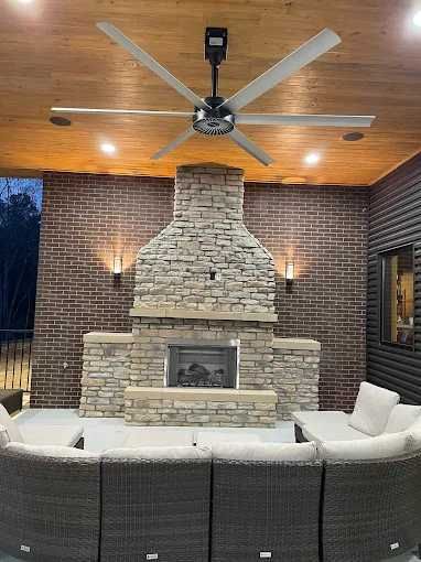 Outdoor seating area with fireplace, brick wall, and large ceiling fan.