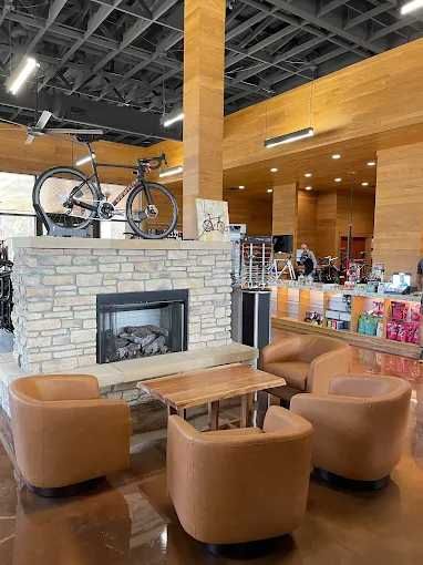 Cozy lounge area in a bike shop with fireplace, chairs, and a bicycle display. Brown tones.