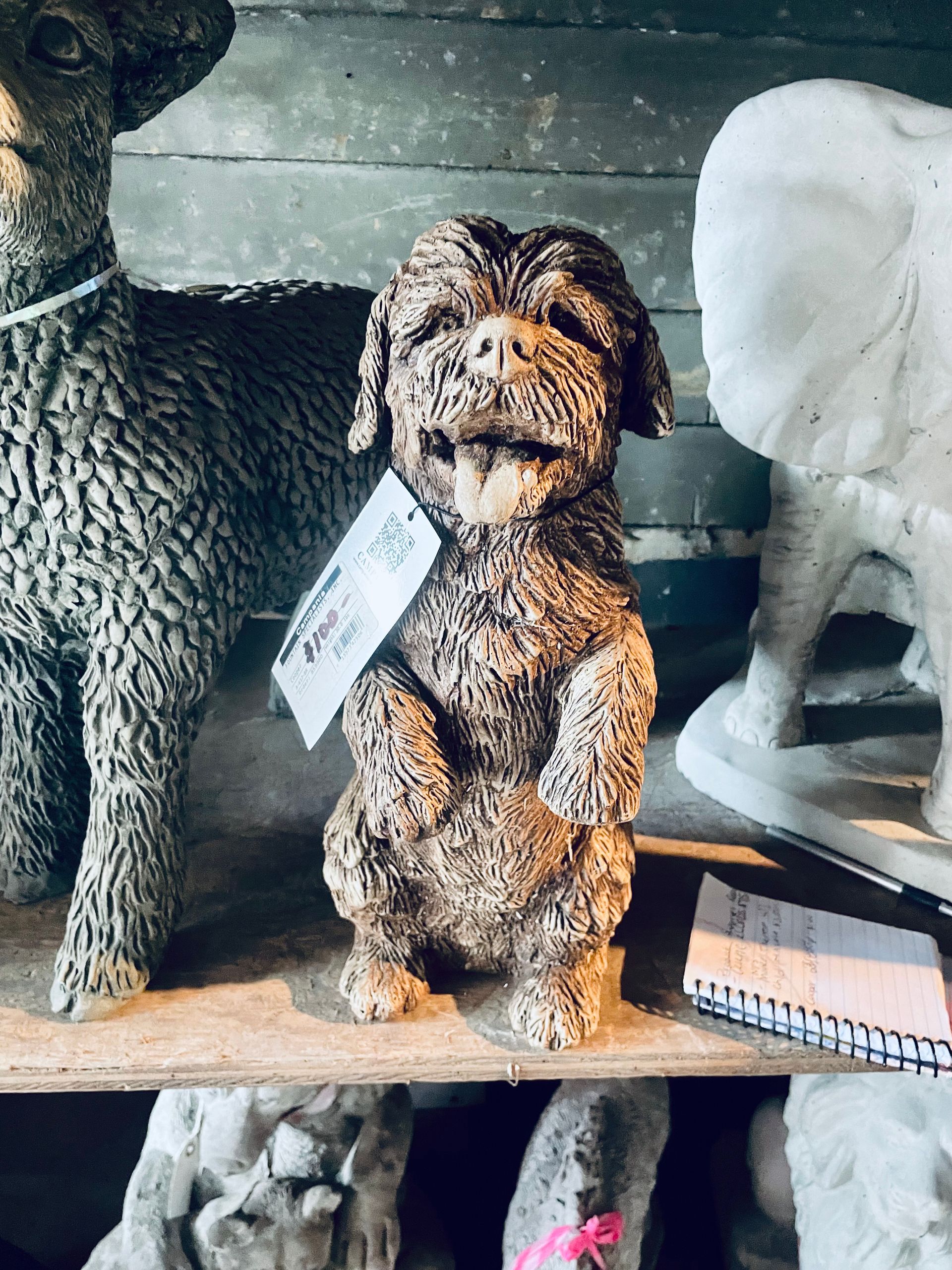 A statue of a dog is sitting on a shelf next to a statue of an elephant.