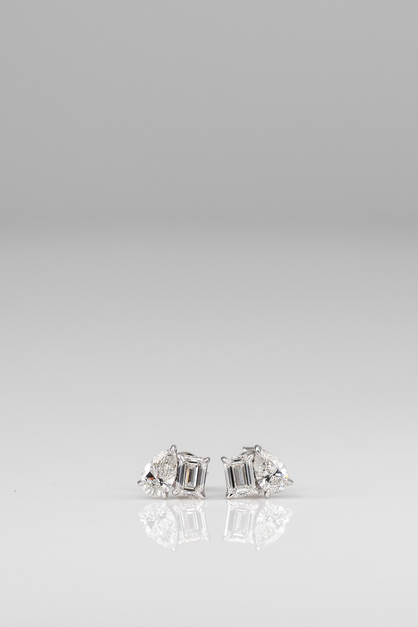 Two small silver decorative objects on a white surface, with subtle reflections below.