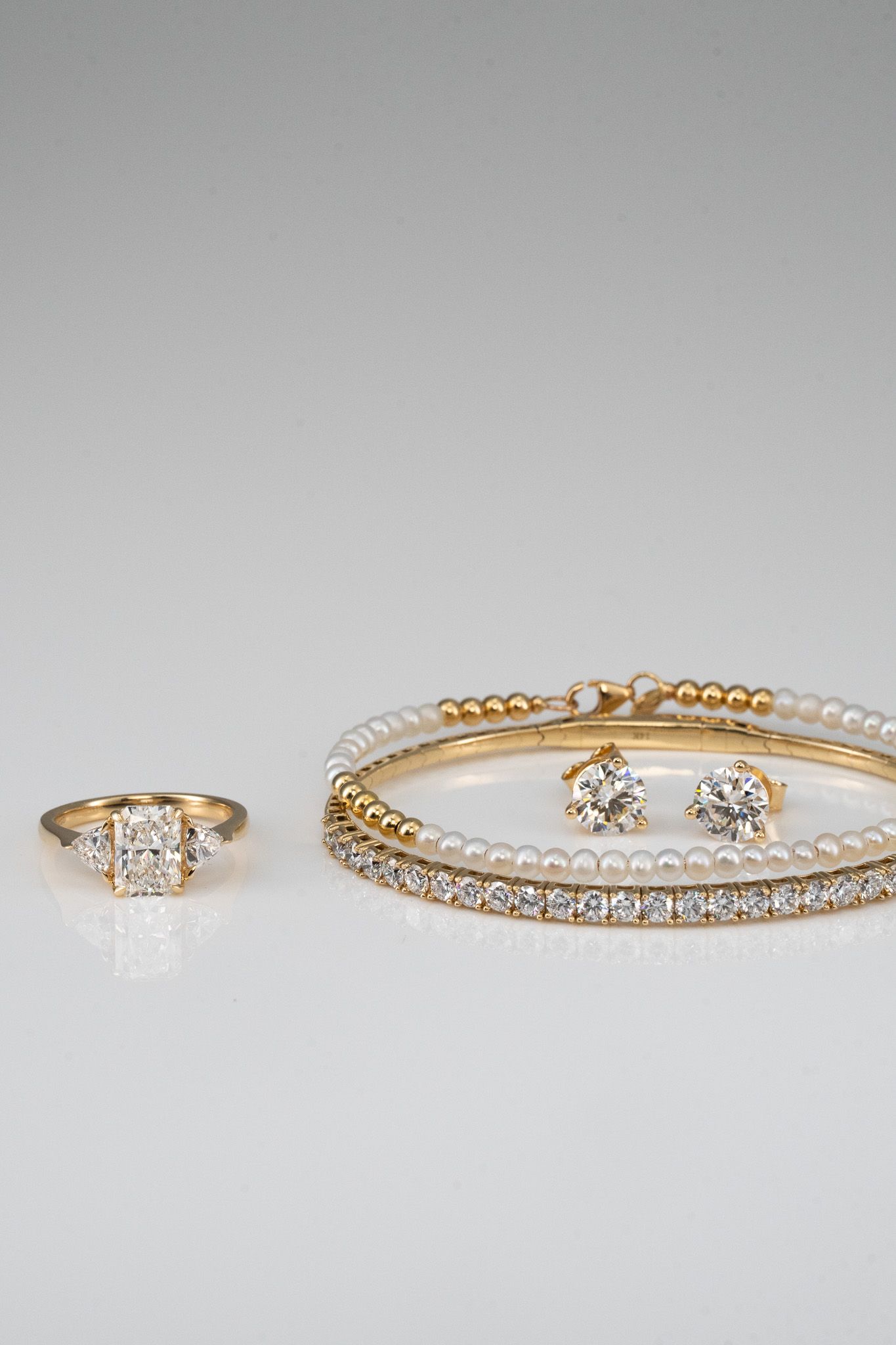 Gold and diamond rings and bracelets arranged on a light gray surface.