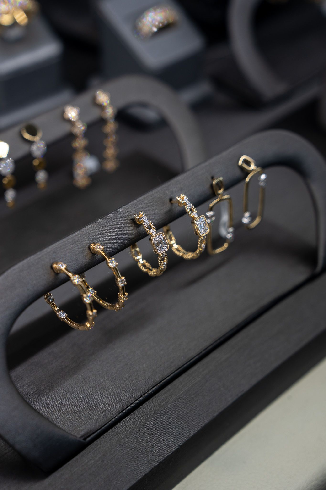 Gold hoop earrings displayed on a black jewelry stand in a store case