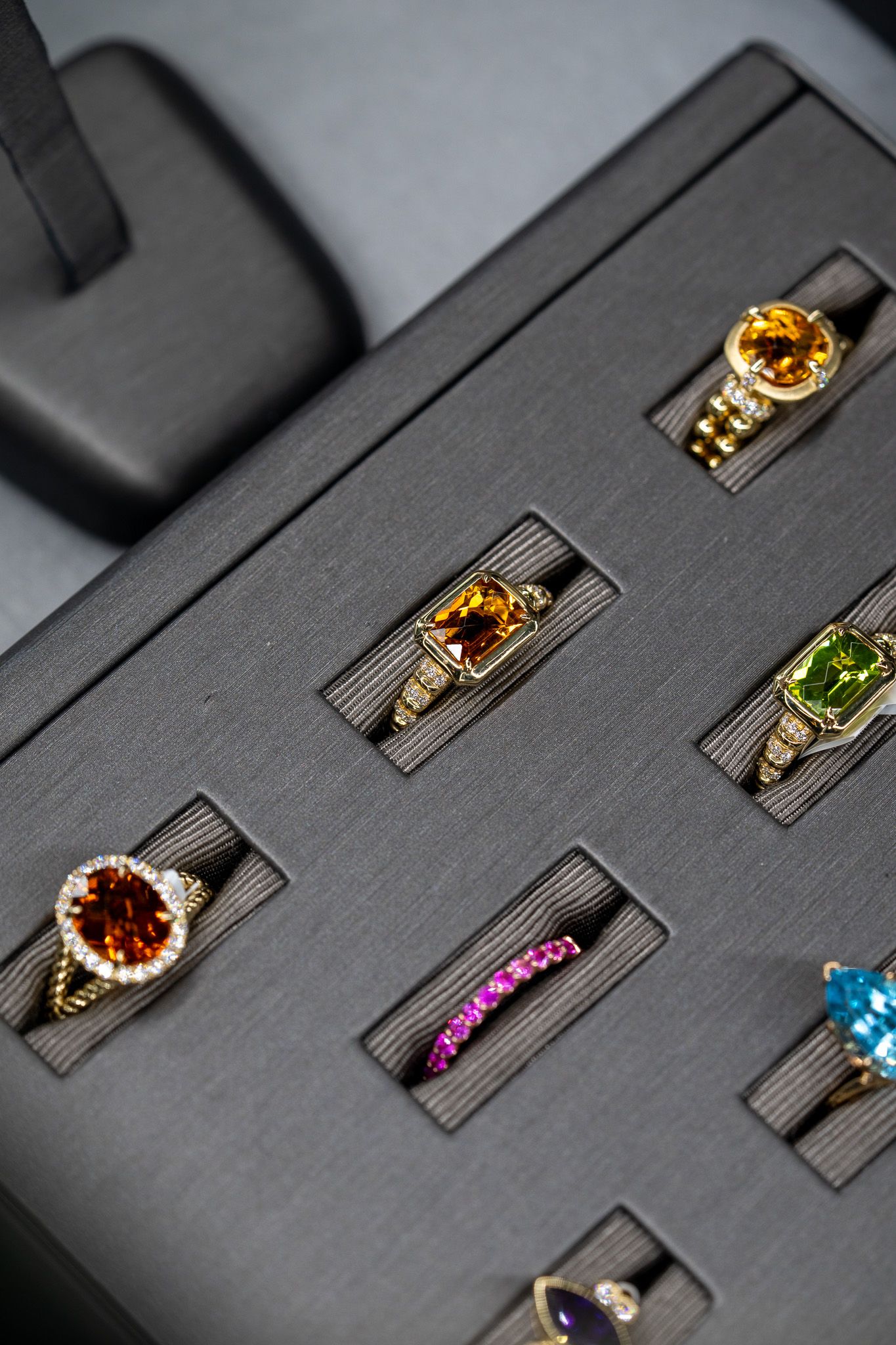 Assorted gemstone rings displayed in a black jewelry case, including amber, green, pink, and blue stones