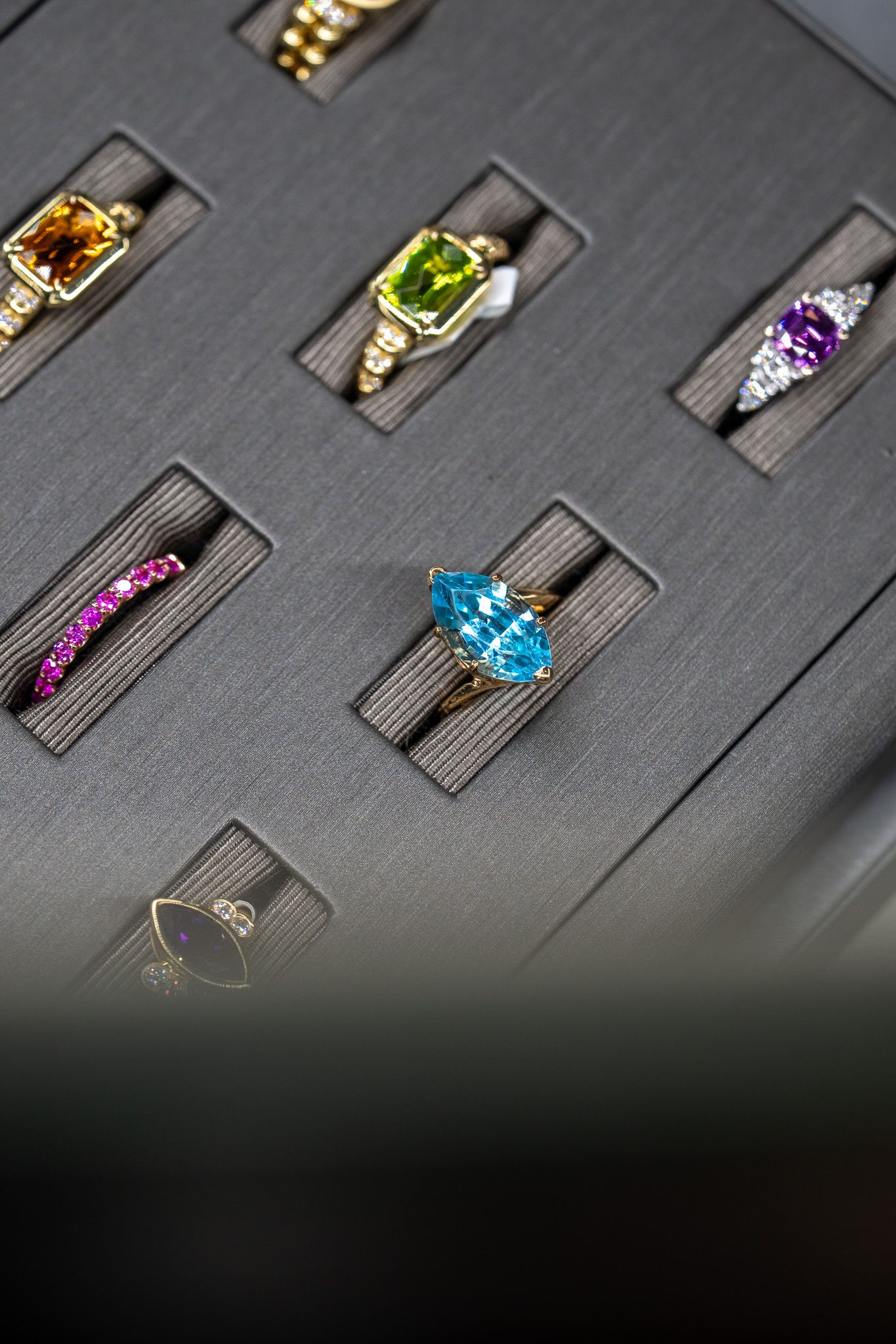 Close-up of assorted colorful gemstone rings displayed in a black jewelry tray.