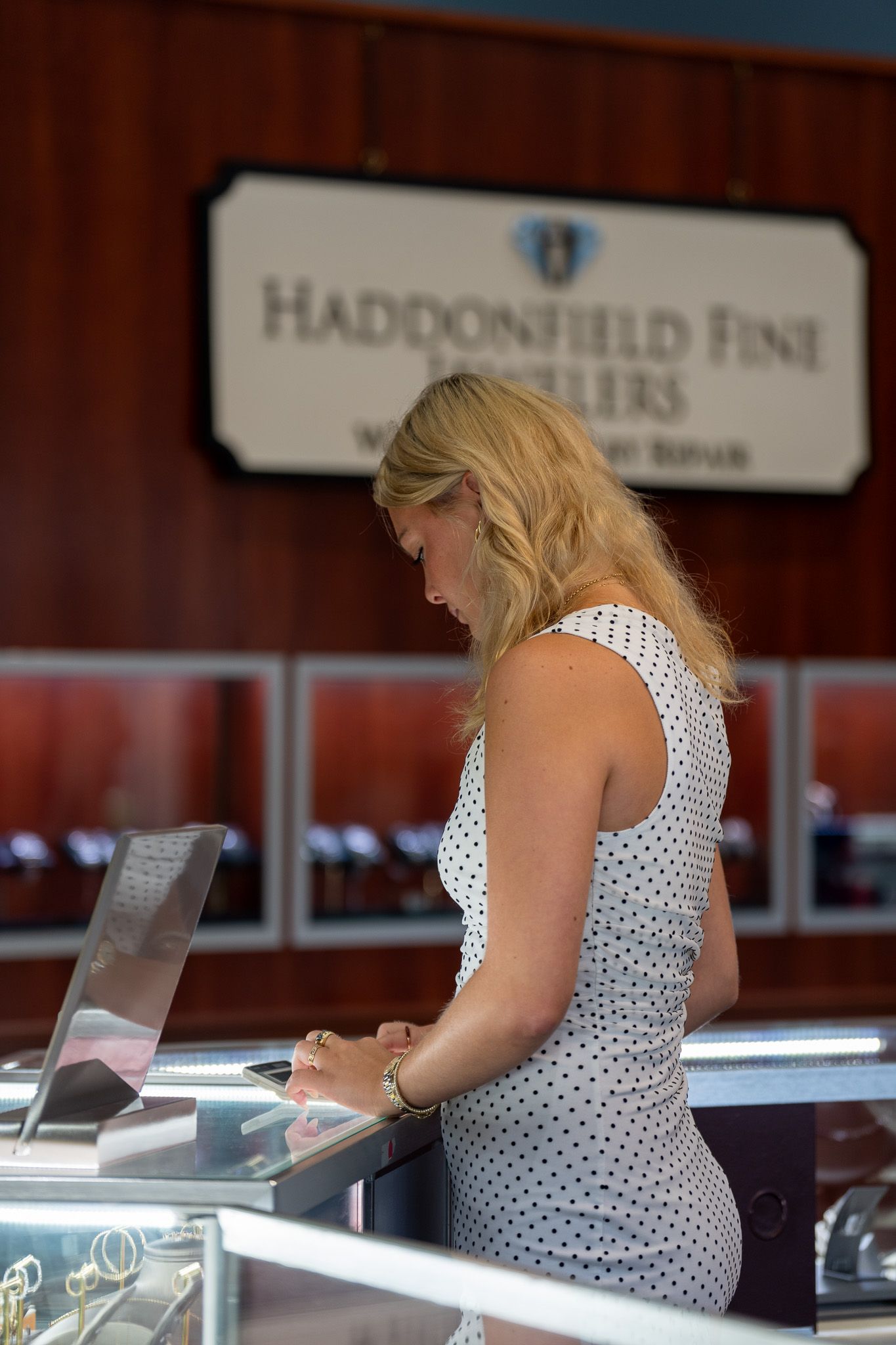 Woman in a white polka-dot dress using a touchscreen at a reception desk, with Haddonfield Fine Arts sign behind her
