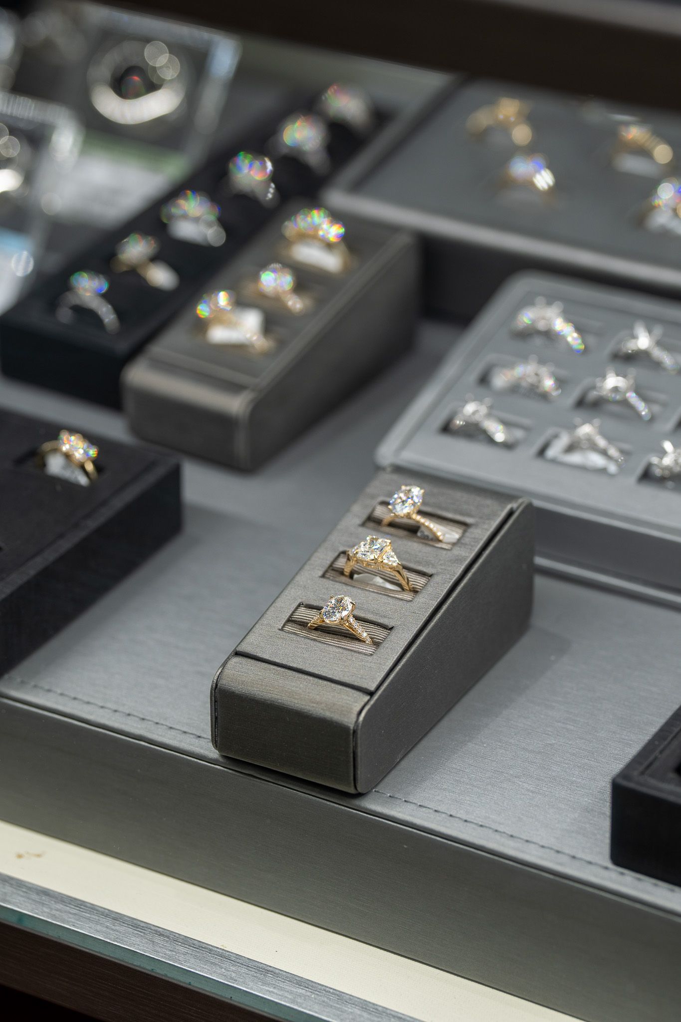 Display trays of jewelry rings on a gray counter, with silver and gold pieces arranged in rows.