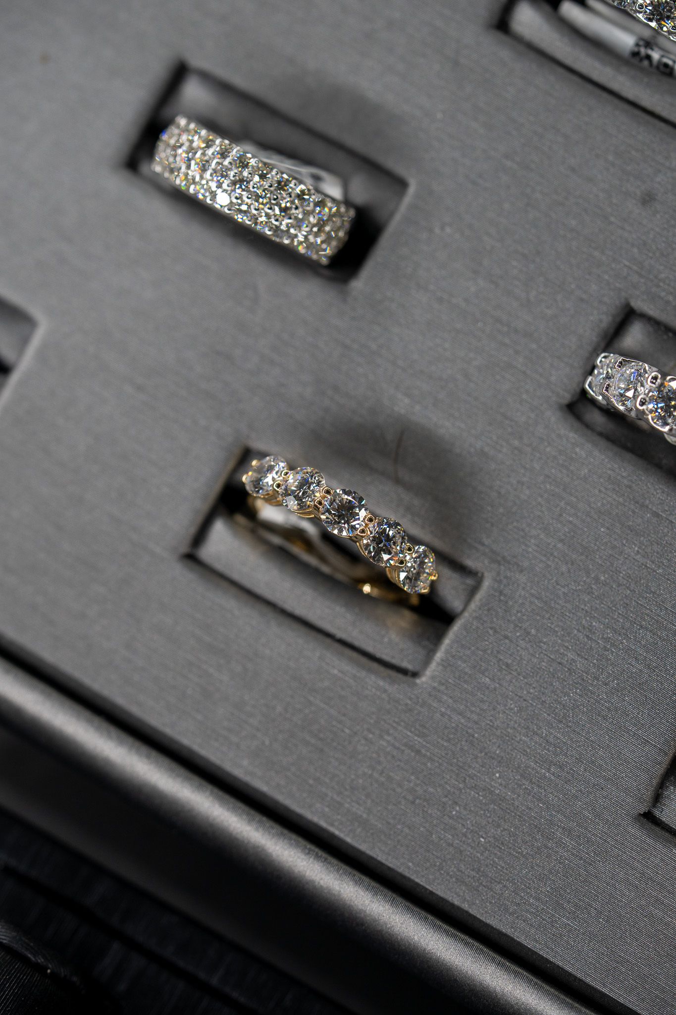 Textured black jewelry case with three ornate silver rings in velvet slots