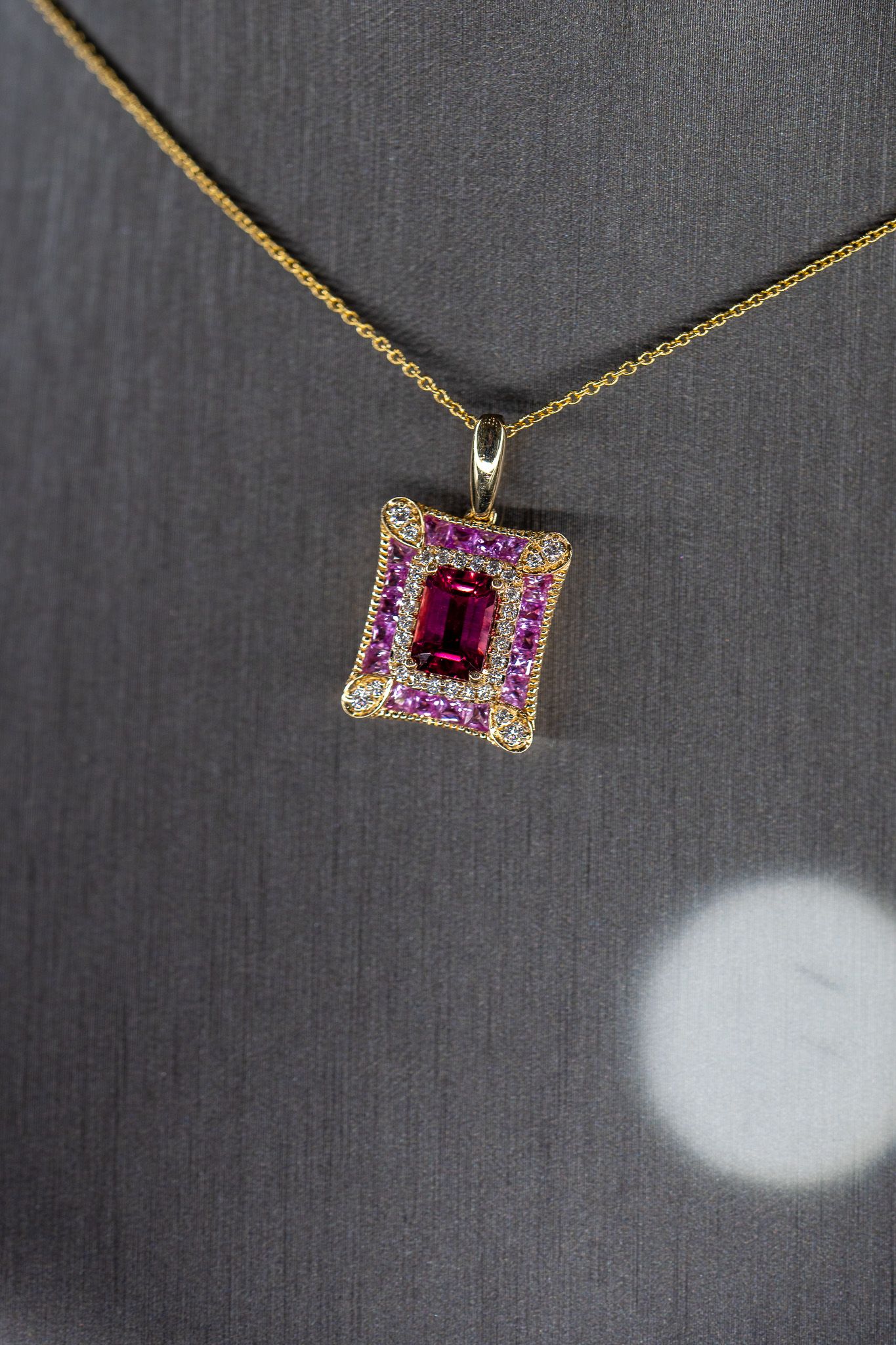 Gold necklace with a pink and clear gemstone pendant on a gray fabric background