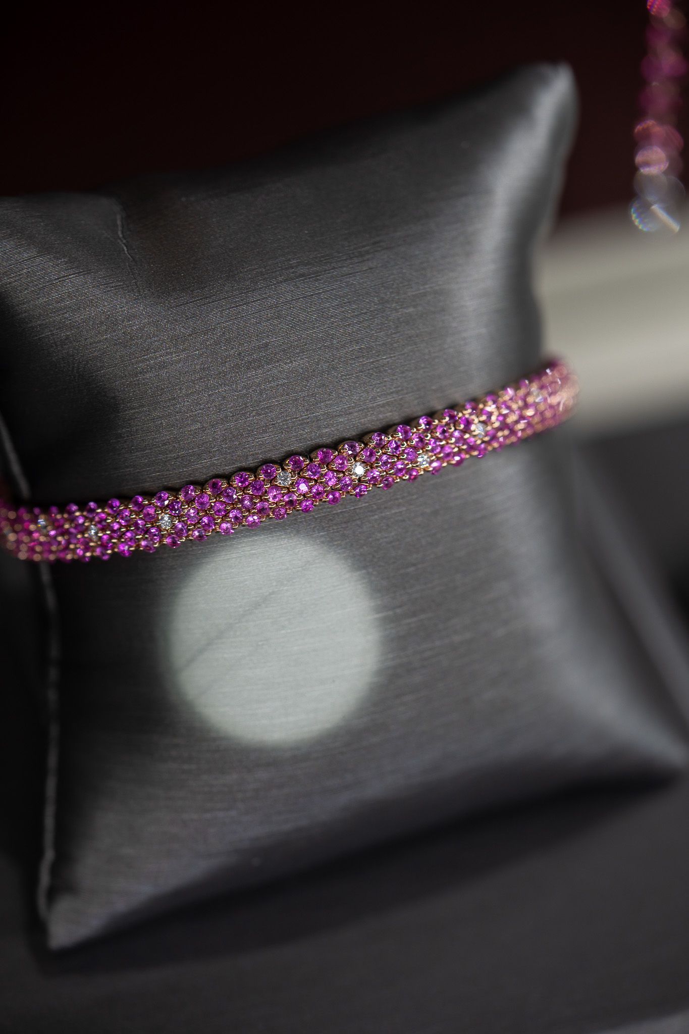 Black leather cushion with a pink-purple beaded band and a round light reflection.