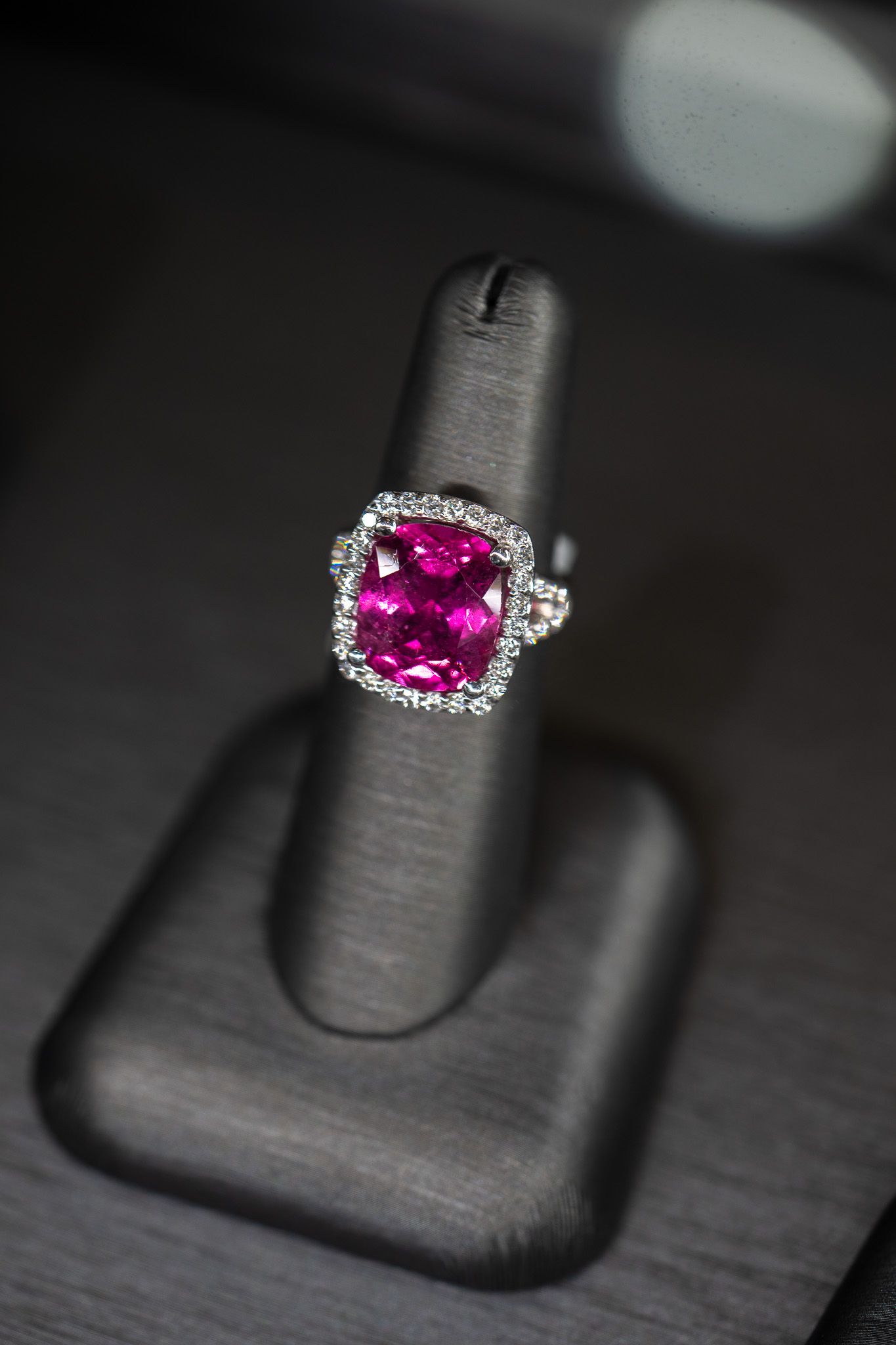 Pink gemstone ring on a black display stand against a dark background