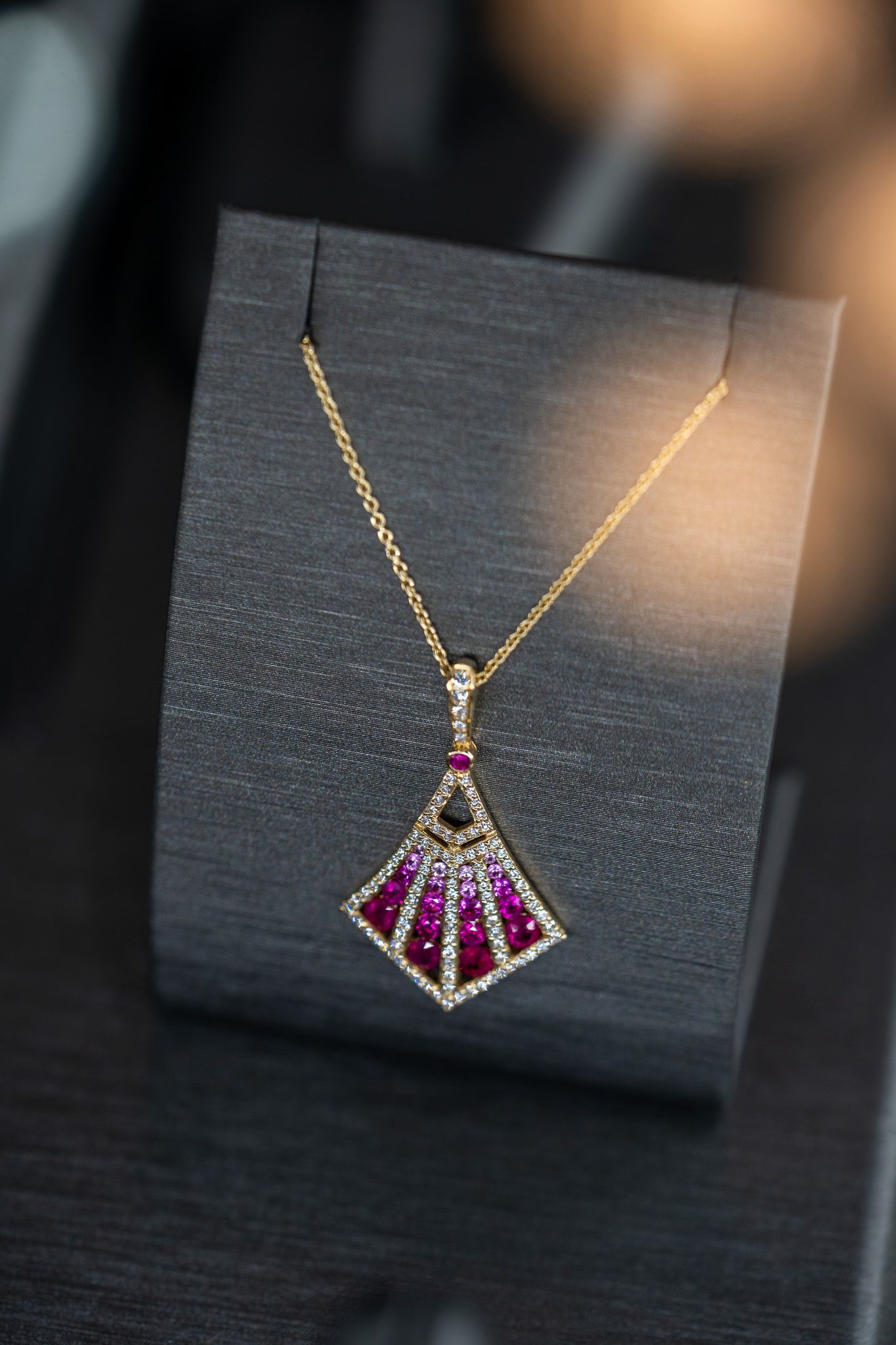 Gold necklace with a purple gemstone pendant on a black display stand