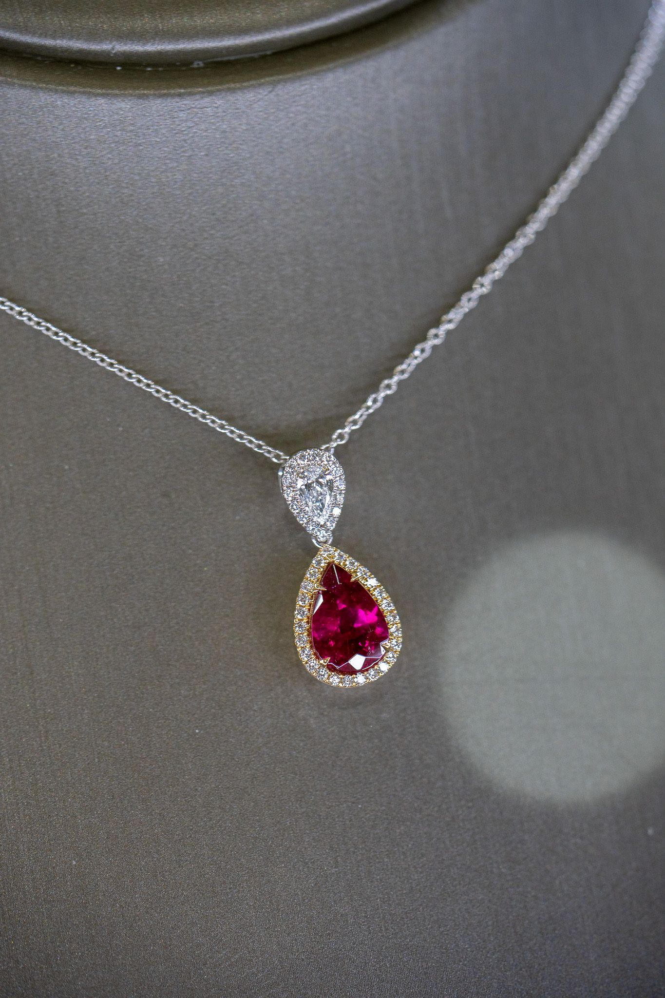 Silver necklace with a red teardrop pendant on a dark display bust