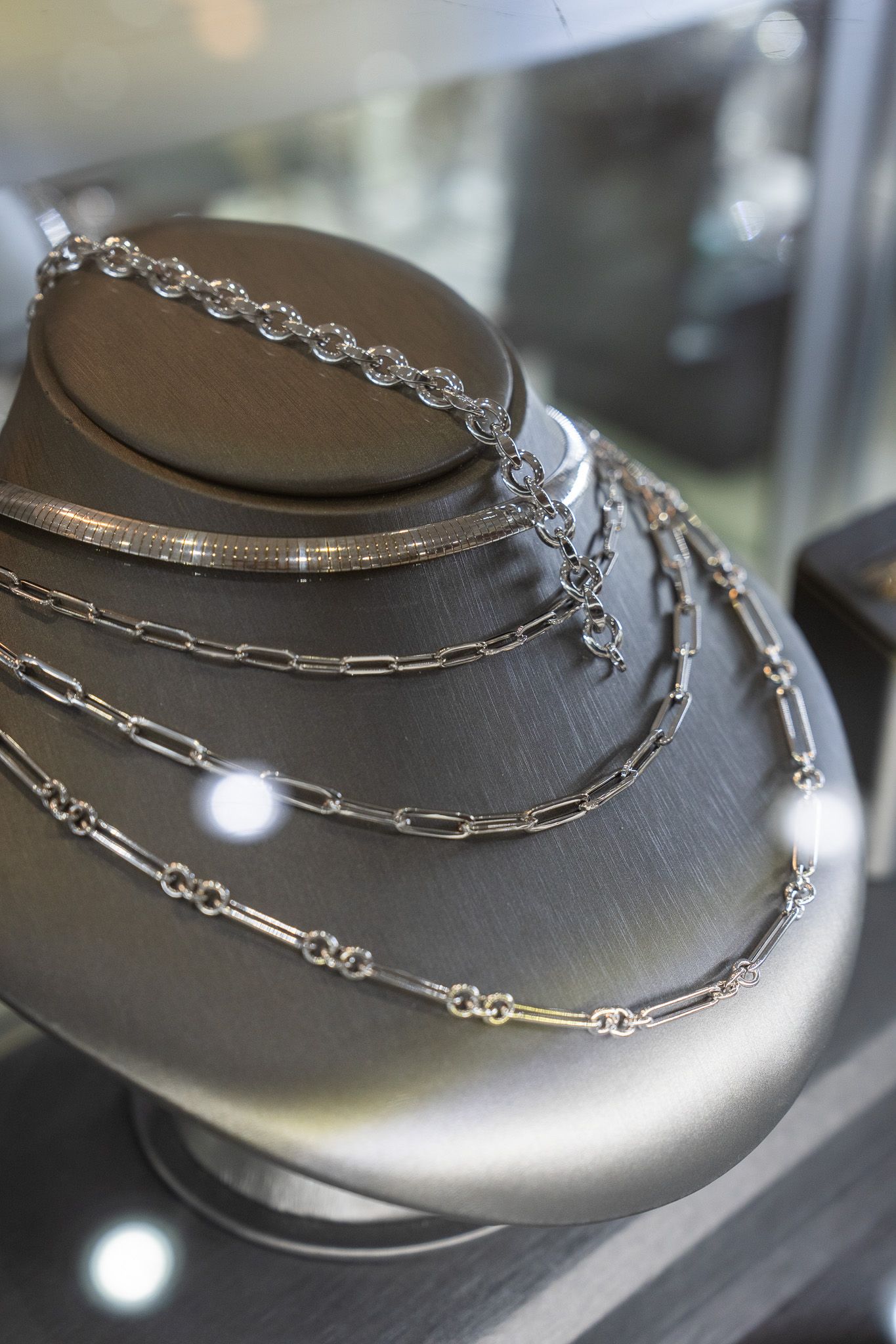 Silver layered necklaces displayed on a black jewelry bust in a store case