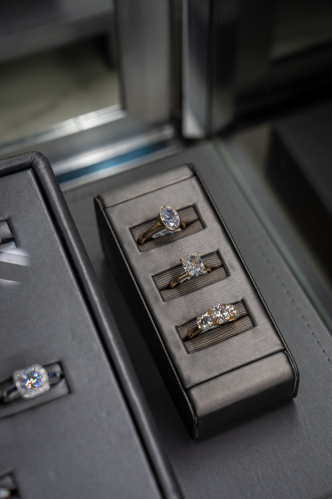 Three rings displayed on a gray velvet jewelry tray next to another ring tray