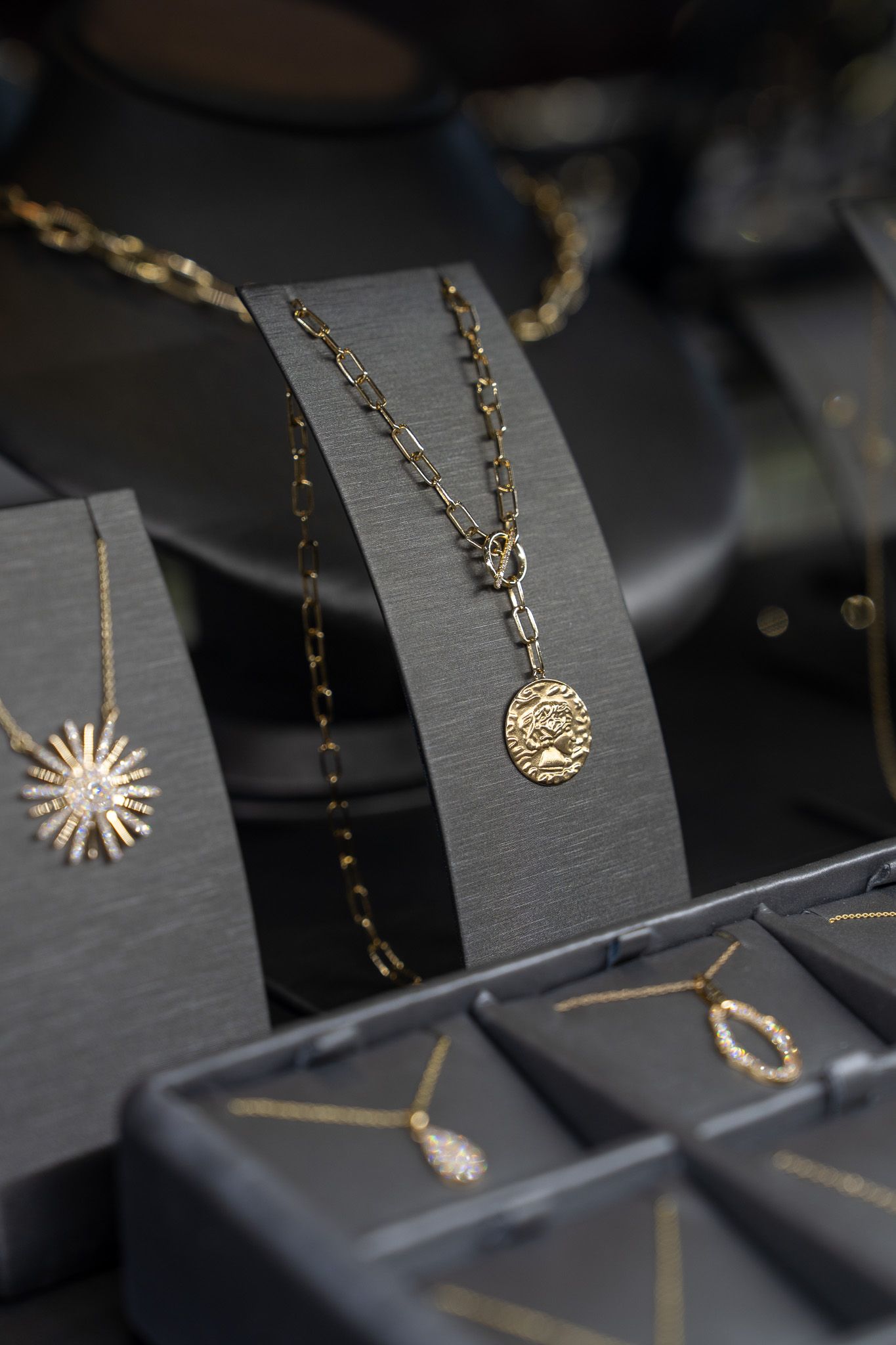 Gold necklaces and pendants displayed on dark velvet jewelry stands and trays.