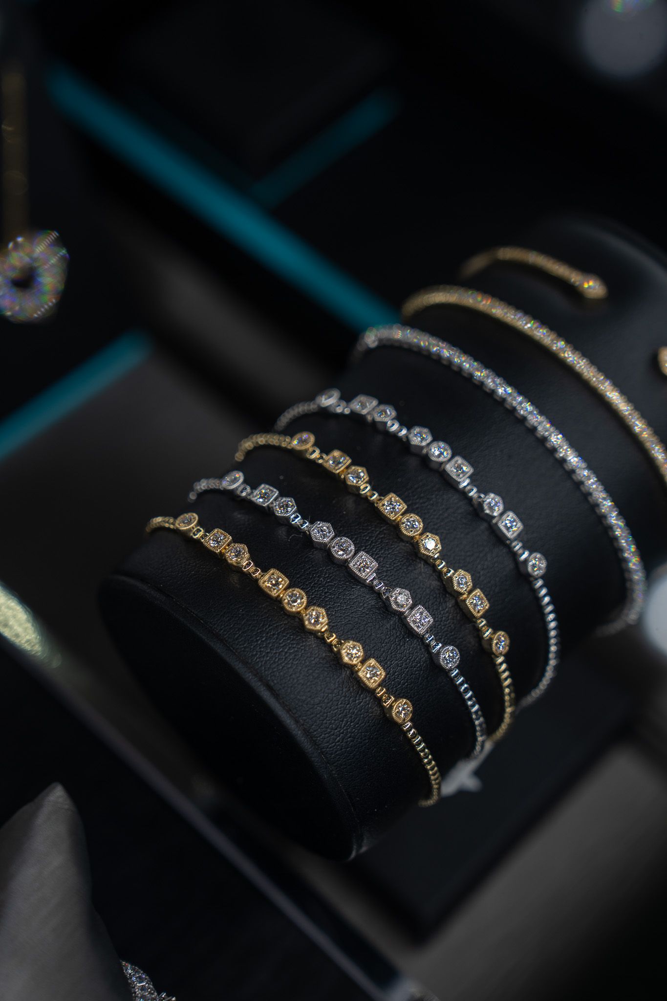 Black display stand with stacked gold and silver chain bracelets on a dark jewelry counter