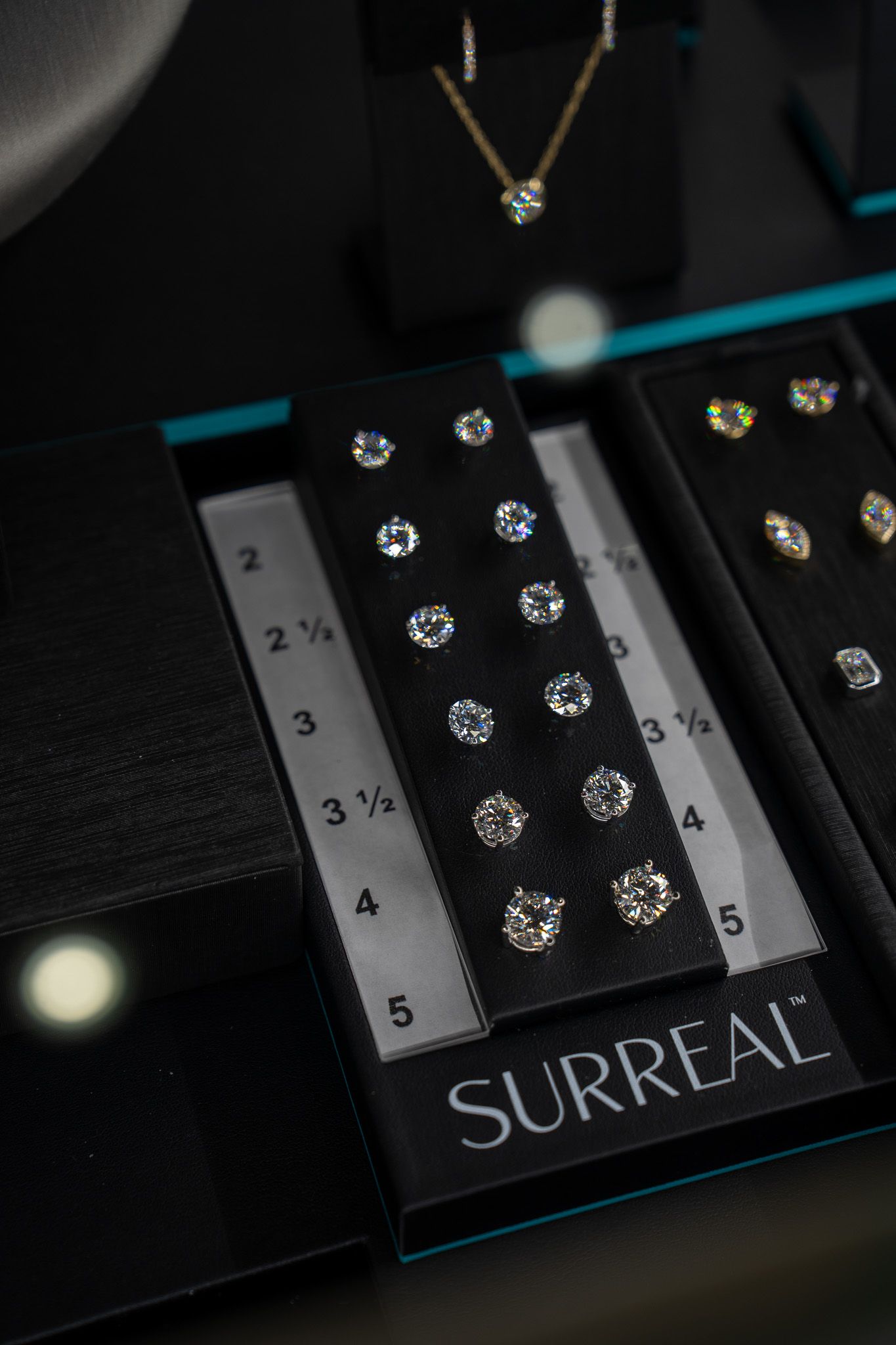 Black necklace with clear gems displayed on a black SURREAL jewelry box with a ruler backdrop