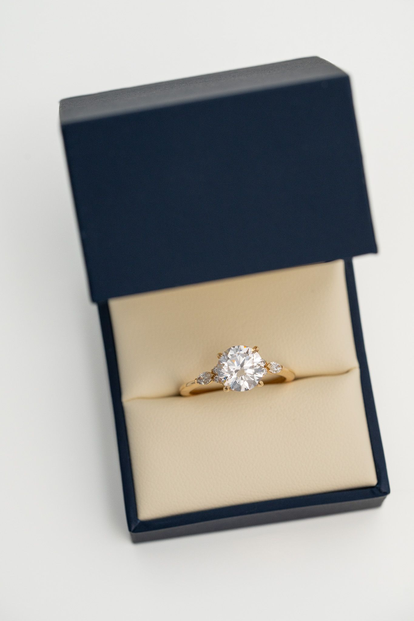 Gold ring with a diamond in a navy jewelry box on a beige cushion