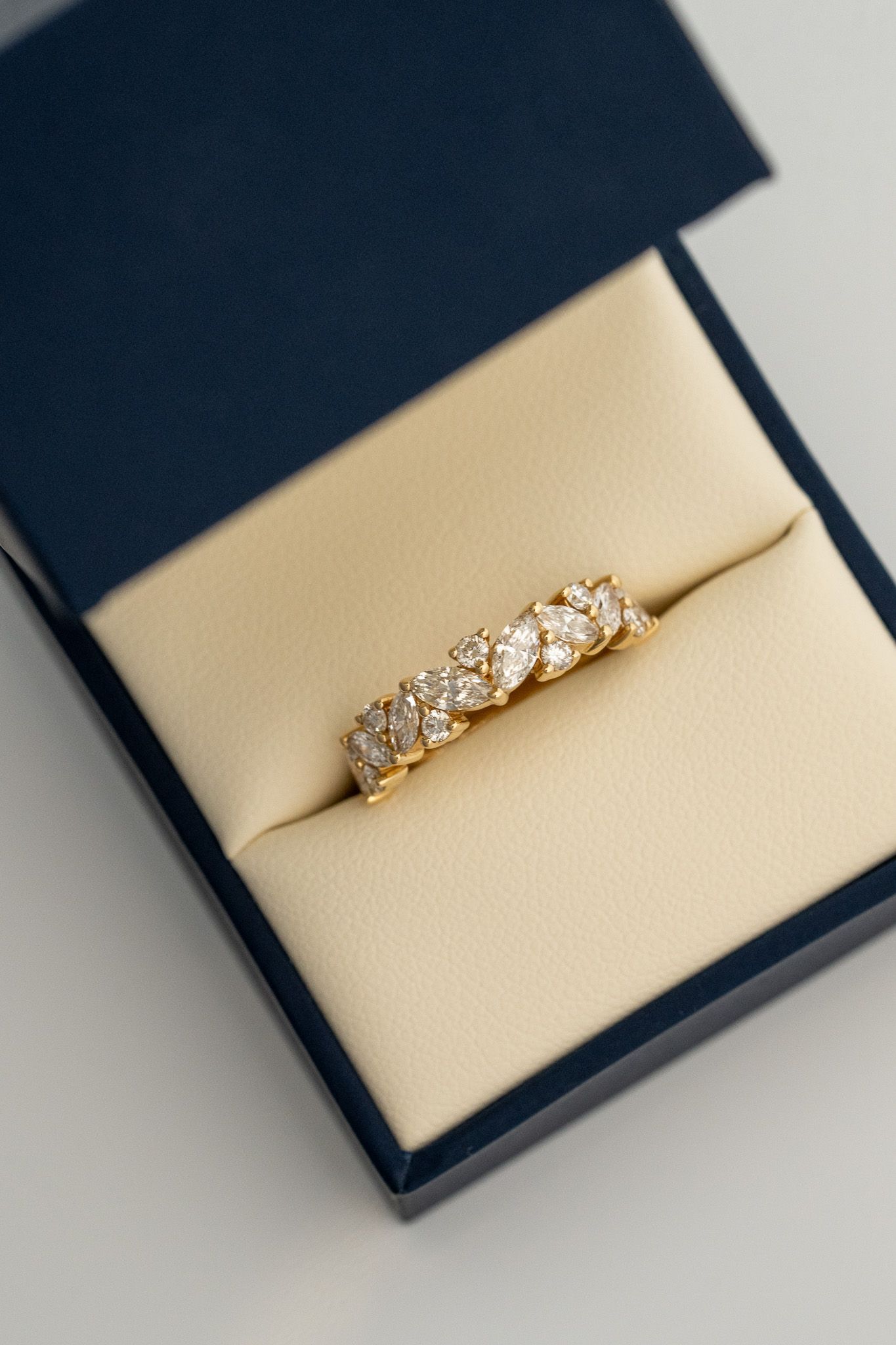 Gold diamond ring in a navy jewelry box on beige velvet cushion