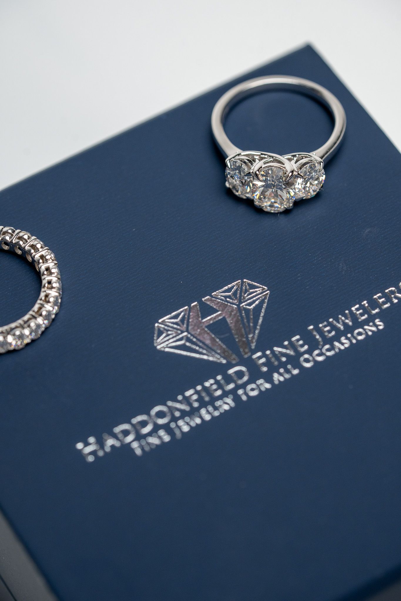 Silver ring with a cluster setting on a navy jewelry box with a logo and branding text