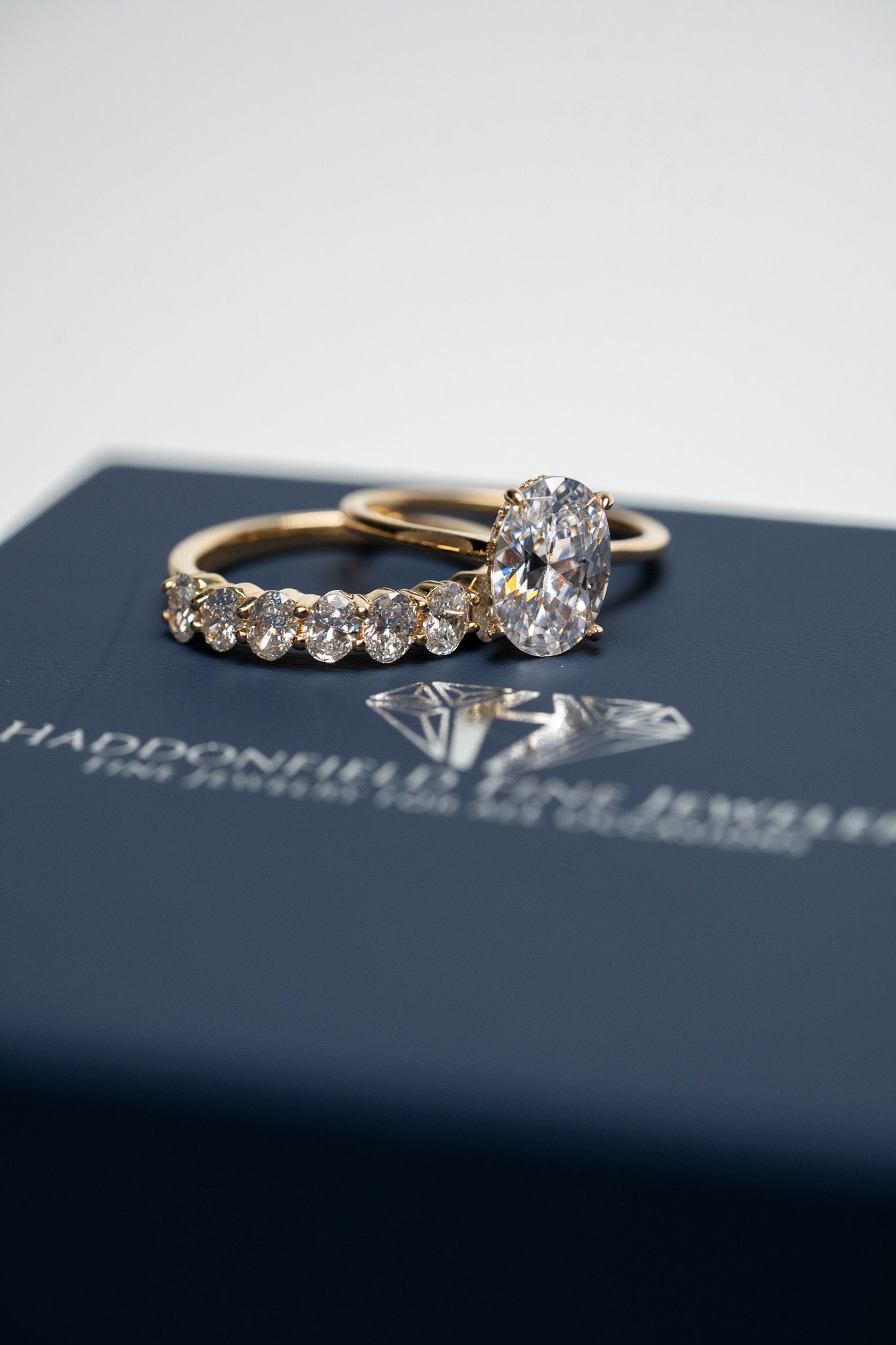 Two gold rings with diamond settings on a dark blue jewelry box