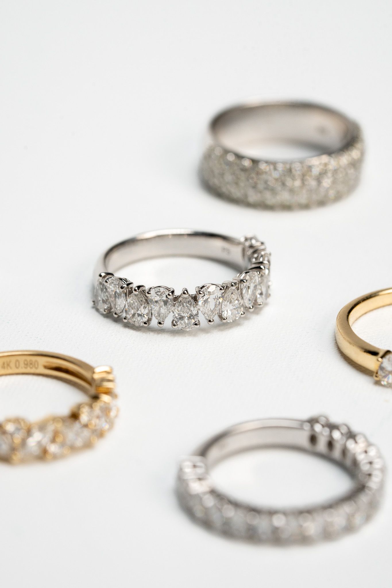 Five diamond-studded rings in silver and gold arranged on a white background