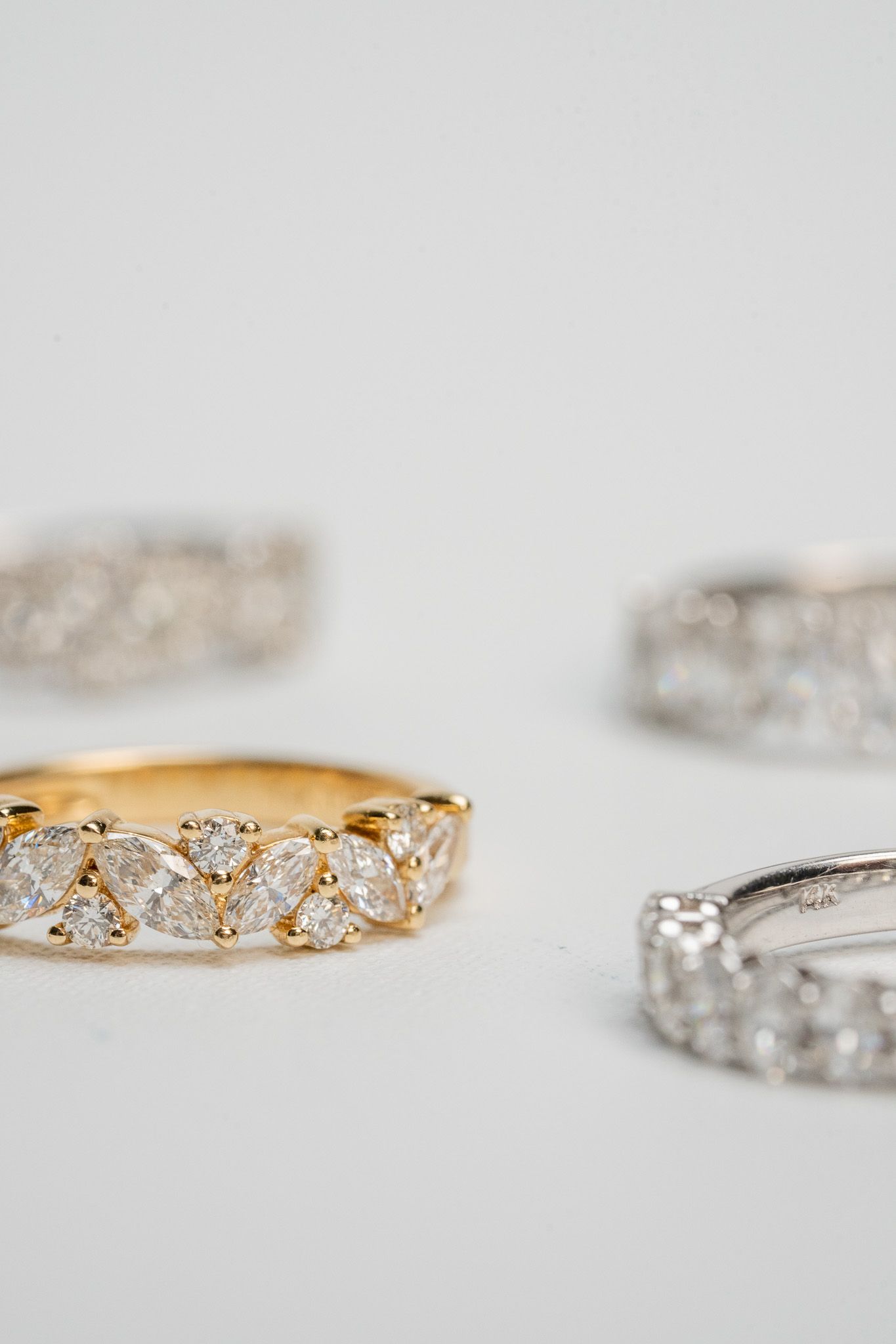 Gold and silver diamond-studded rings displayed on a soft gray background