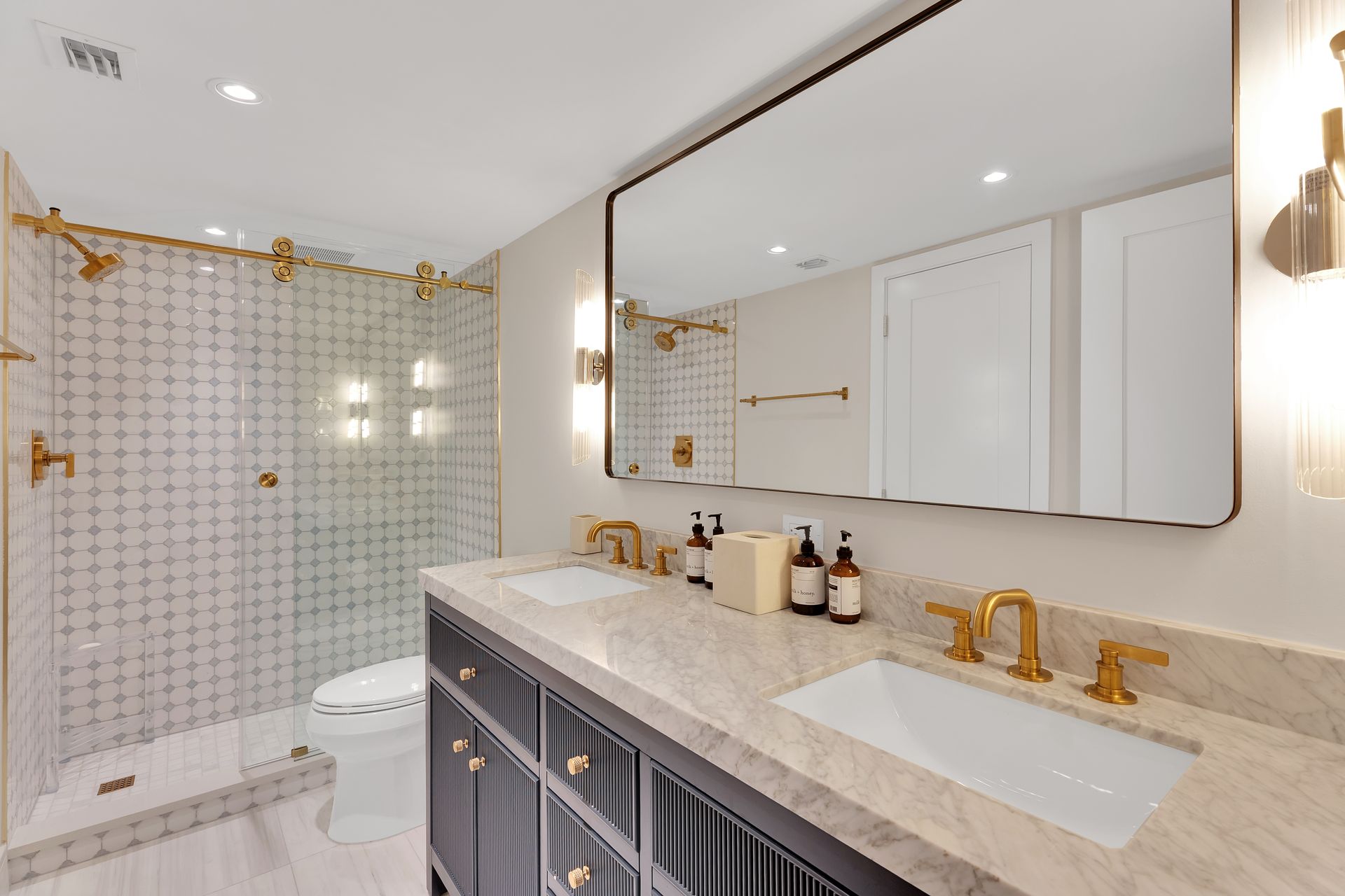 Bright modern bathroom with glass shower, double vanity, and gold fixtures