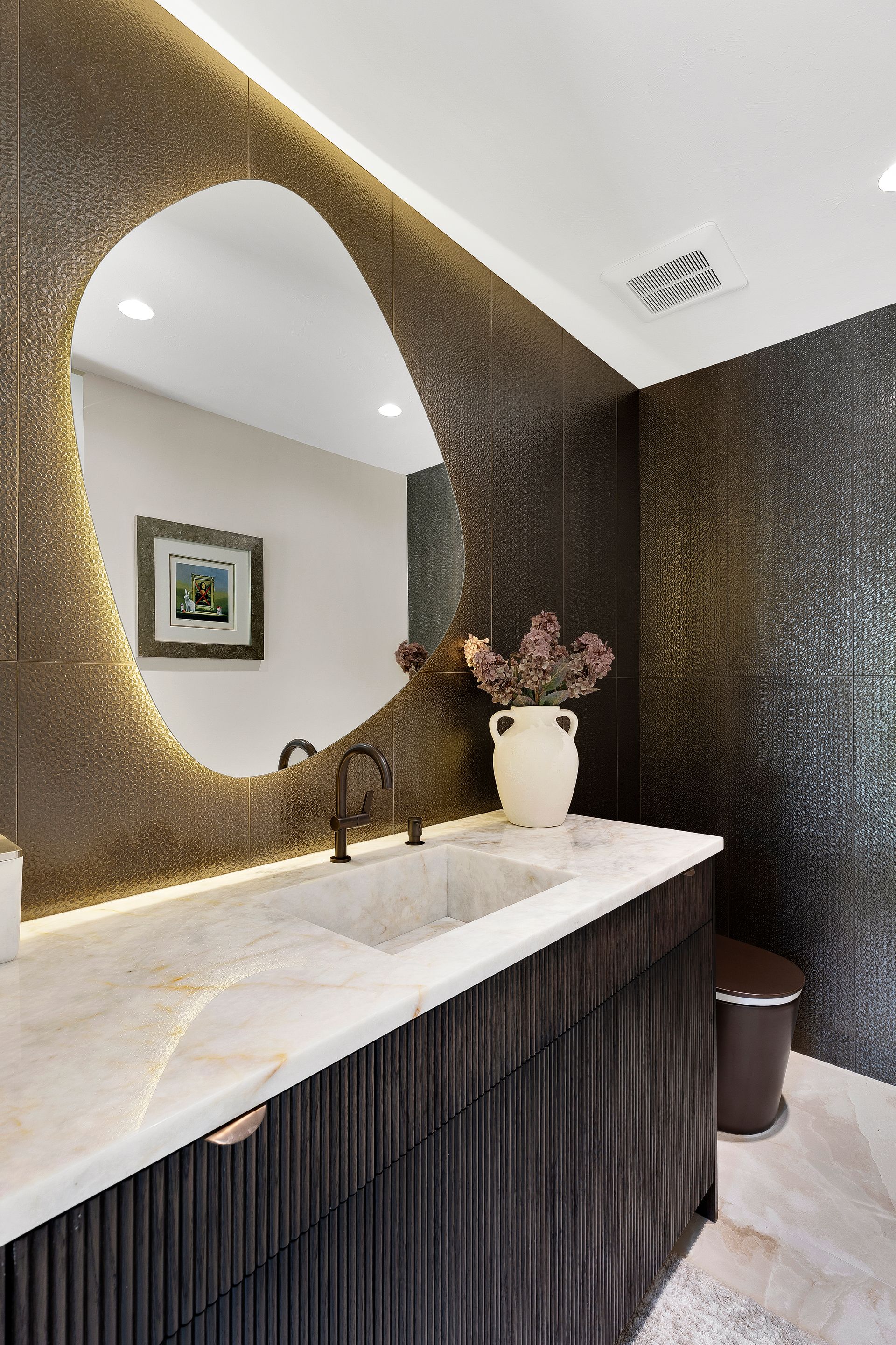 Modern bathroom vanity with oval mirror, dark textured walls, and white marble countertop