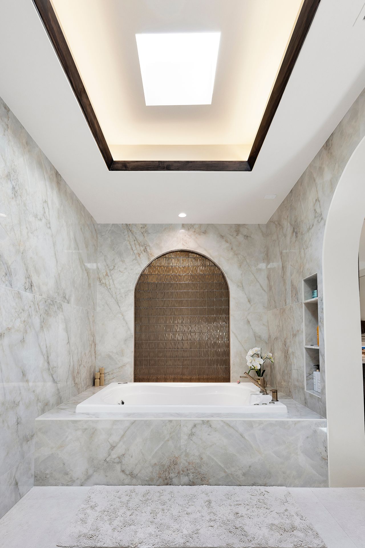 Marble bathroom with a freestanding tub, arched niche, and skylight ceiling
